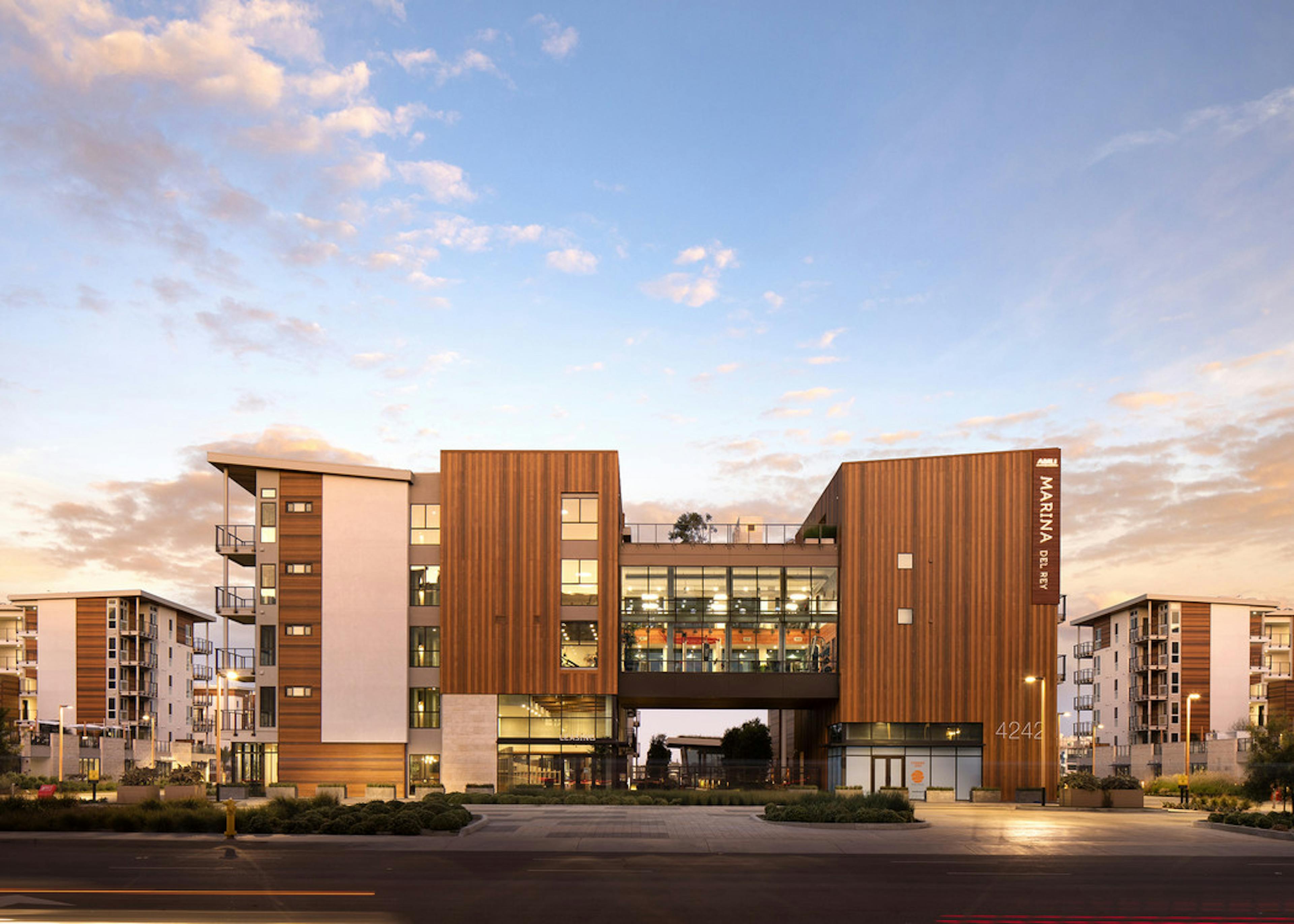 Exterior daytime rendering of AMLI Marina Del Rey apartment building's front entrance wood-paneling facade and lush landscape