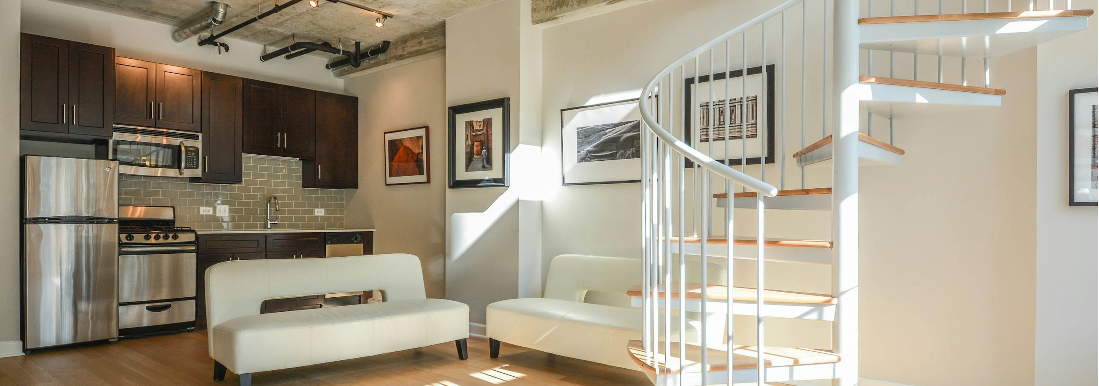 Live work interior at AMLI Evanston with white leather couches and a wrap around staircase with kitchen visible in the back