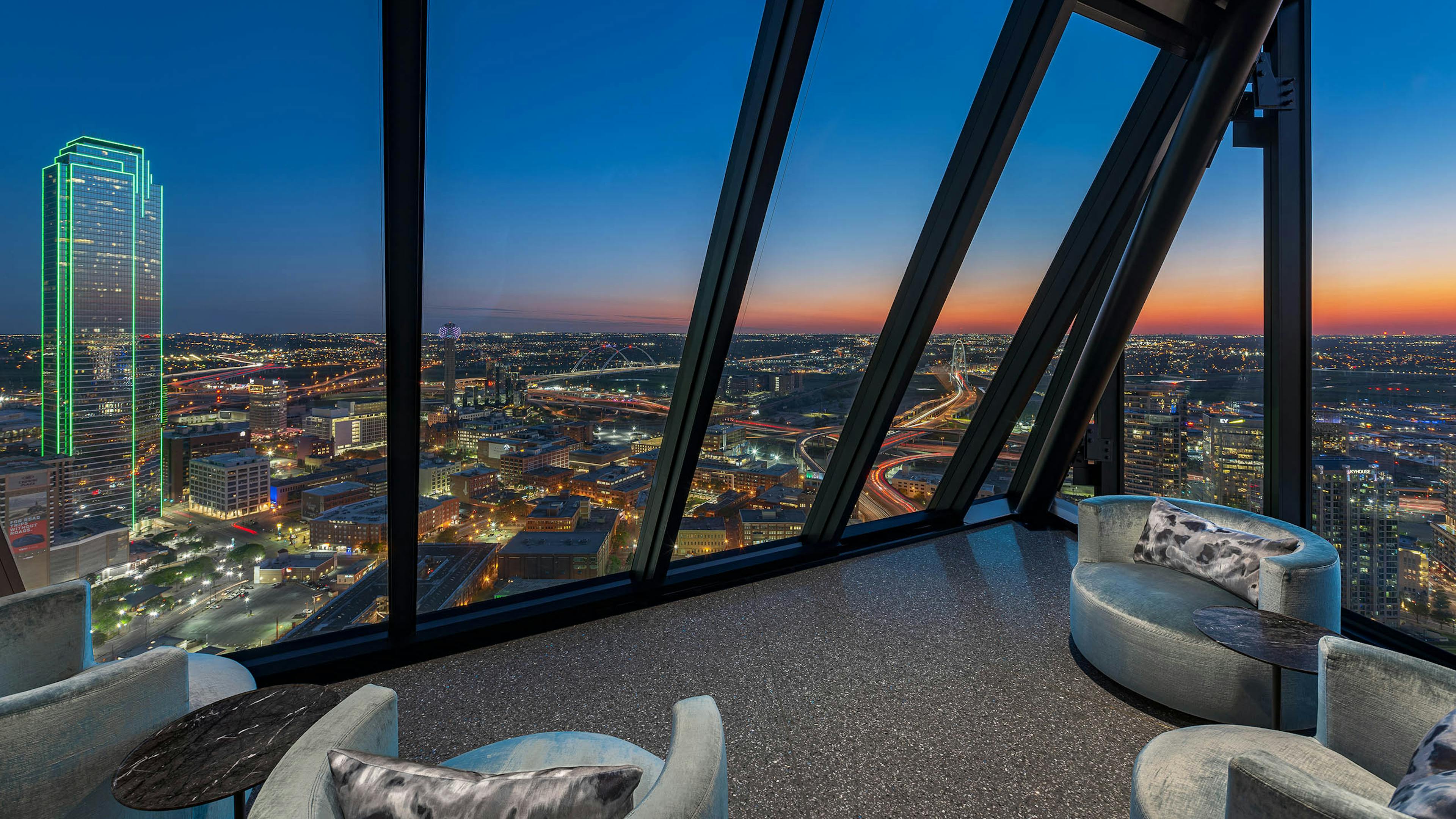 AMLI Fountain Place sky lounge with 4 silver velvet chairs and side tables overlooking the downtown Dallas skyline at dusk