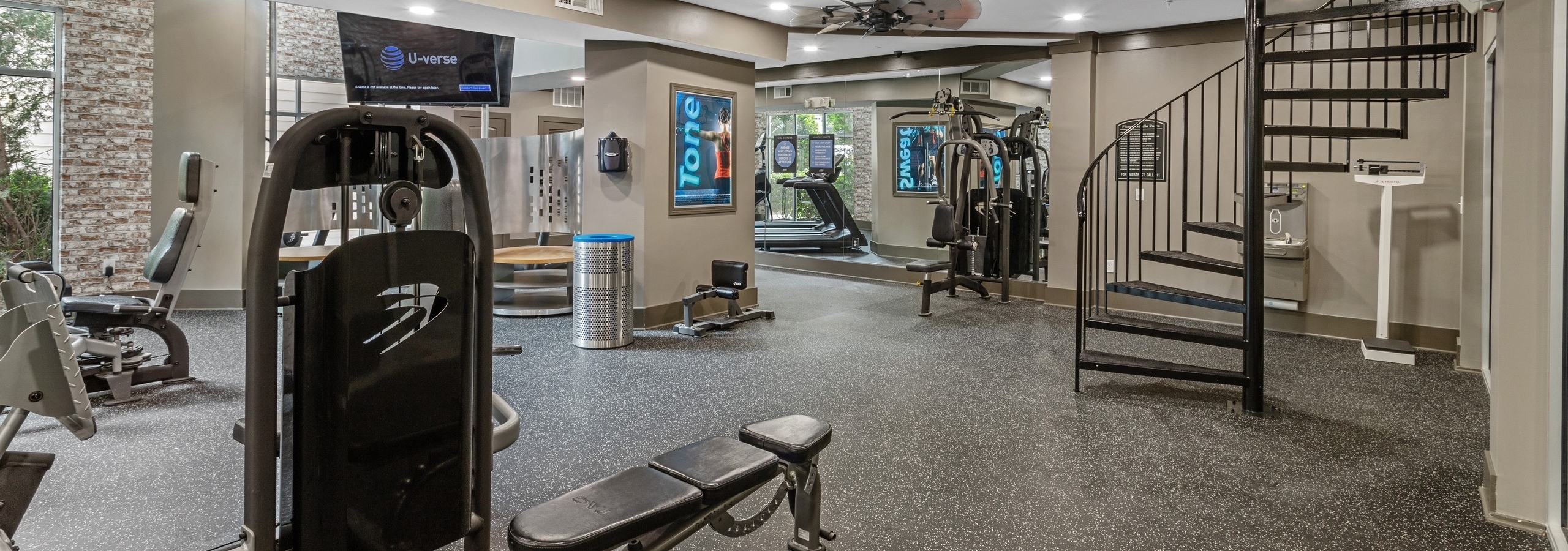 Interior view of AMLI North Point fitness center with weight machines and ceiling fan and hanging TVs with spiral staircase