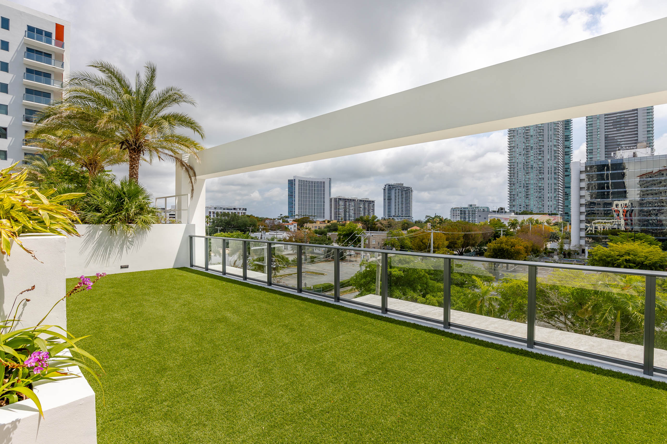 The roof top terrace at AMLI Midtown Miami apartments with faux grass floor surrounded by glass fence panels and city view  