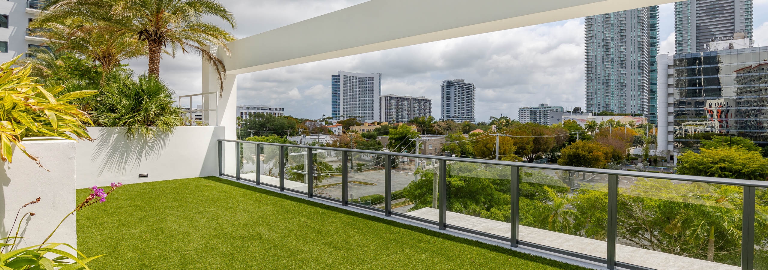 The roof top terrace at AMLI Midtown Miami apartments with faux grass floor surrounded by glass fence panels and city view