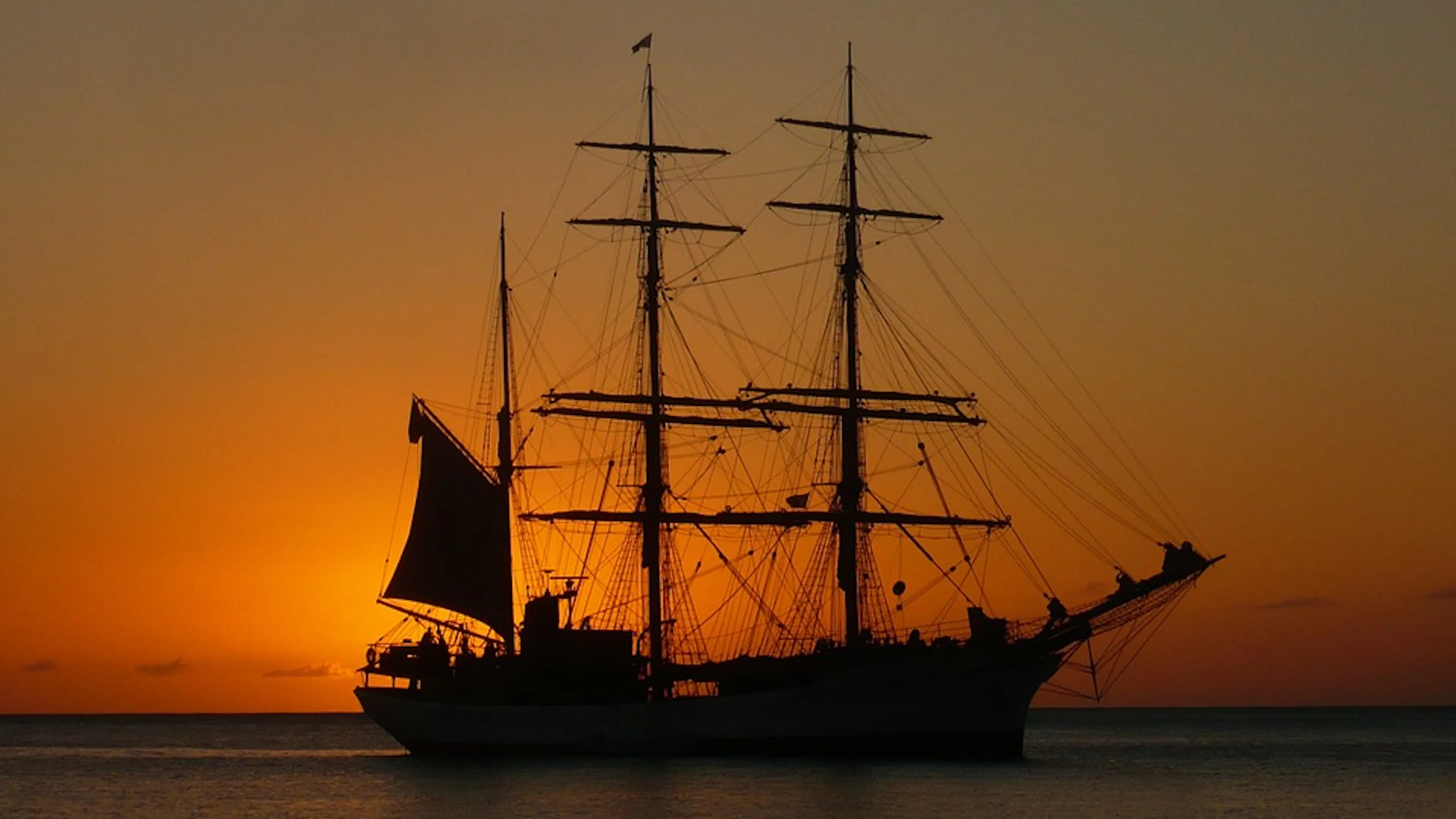 A pirate ship silhouette on calm waters against a bright orange sunset