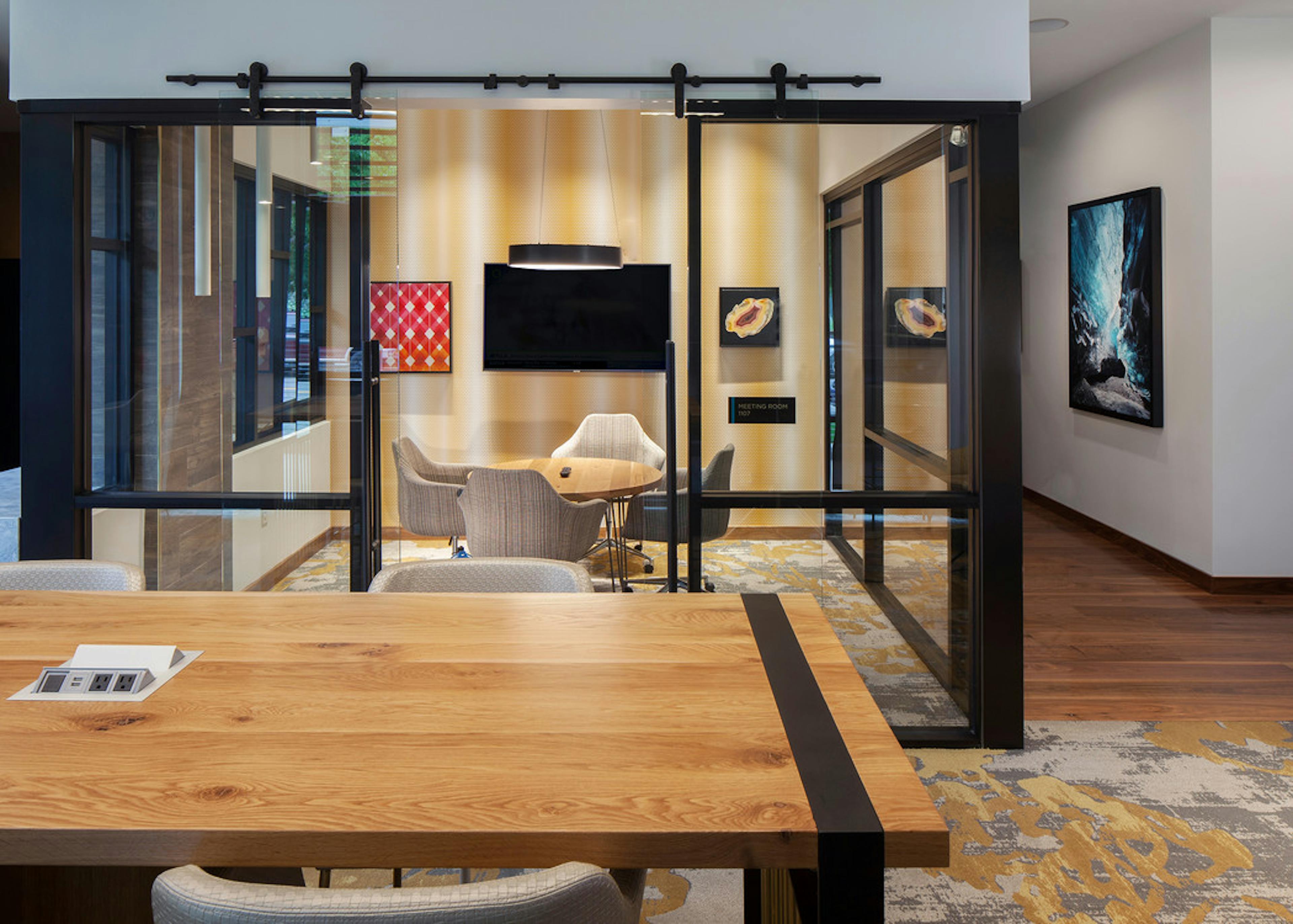 A conference room at AMLI Riverfront Green apartments with wooden table and chairs with view into separate presentation room