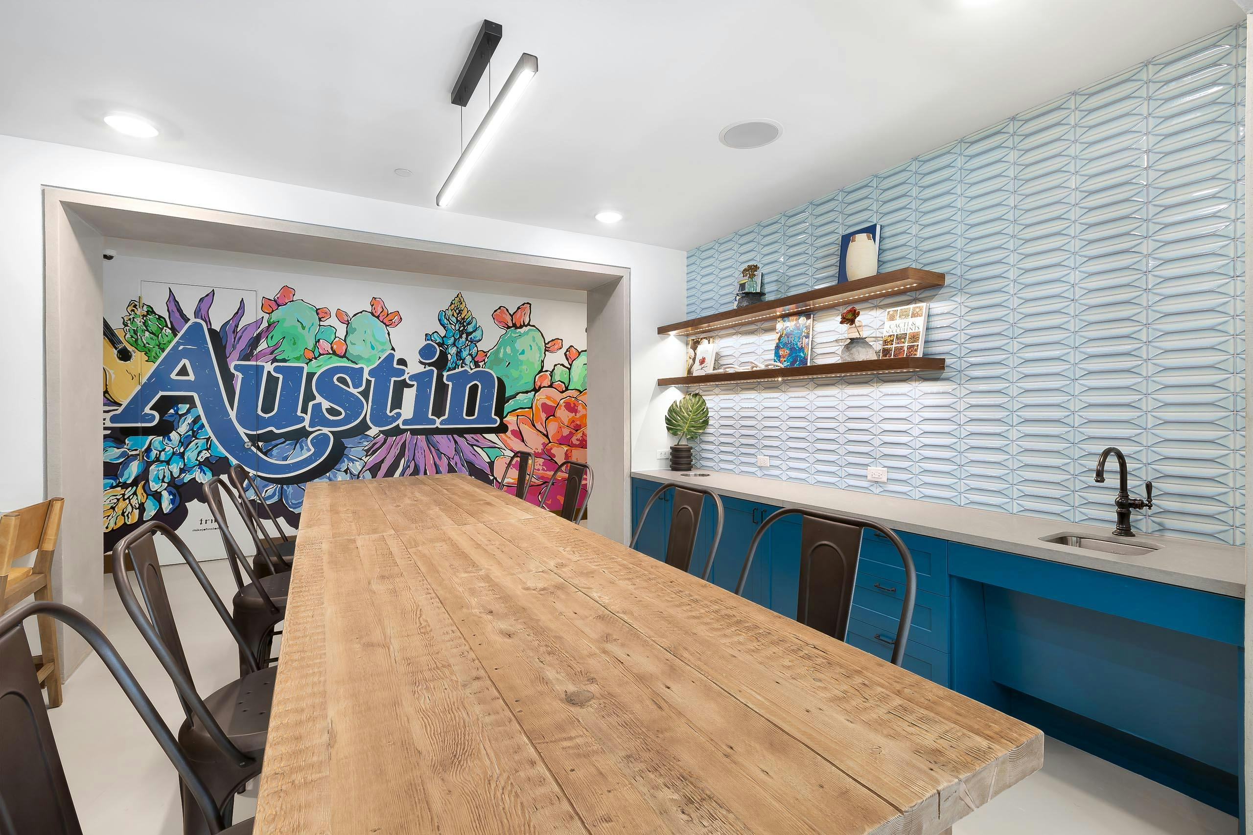 AMLI Lakeline maker space with a colorful Austin mural and a long wooden table flanked by metal chairs and blue cabinetry