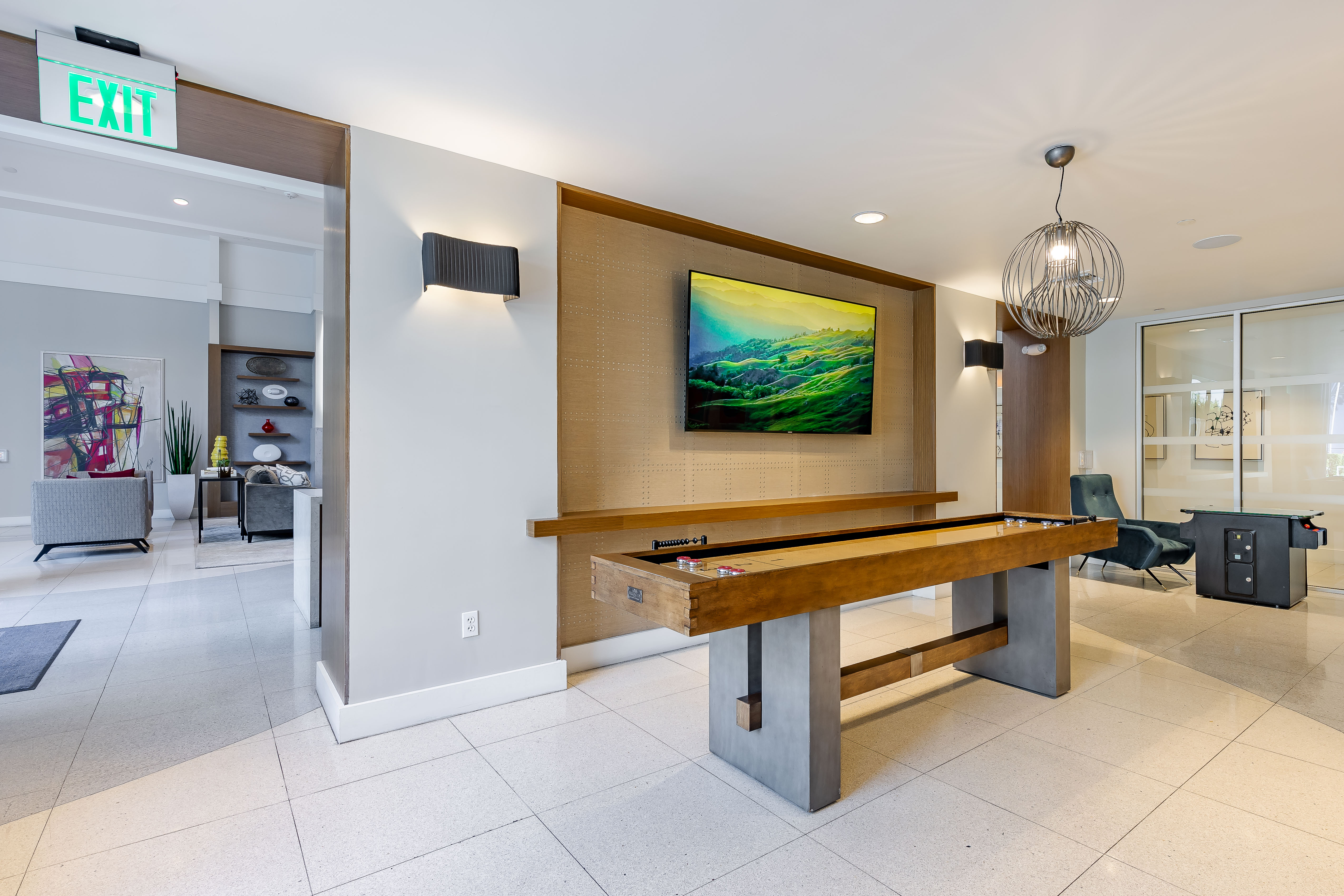 The game room at AMLI 8800 apartments with a wooden shuffleboard table and TV on the wall and a metal chandelier 