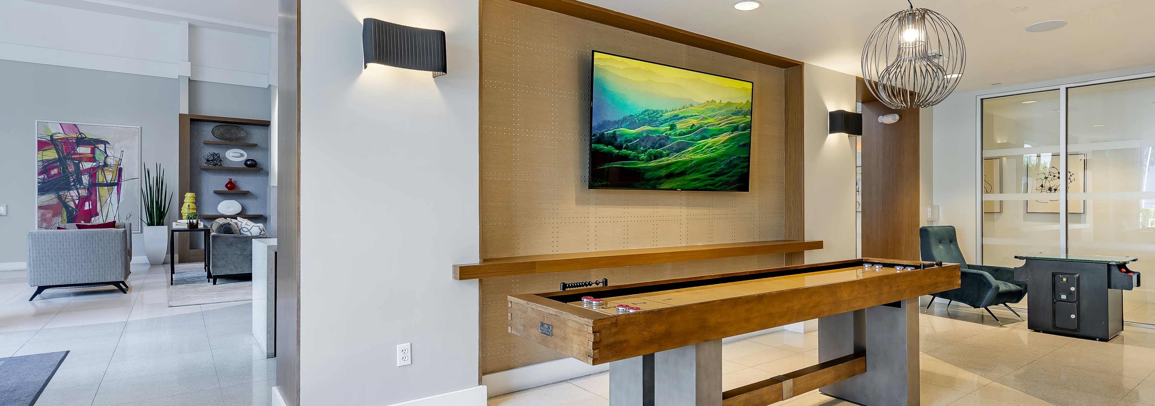 The game room at AMLI 8800 apartments with a wooden shuffleboard table and TV on the wall and a metal chandelier