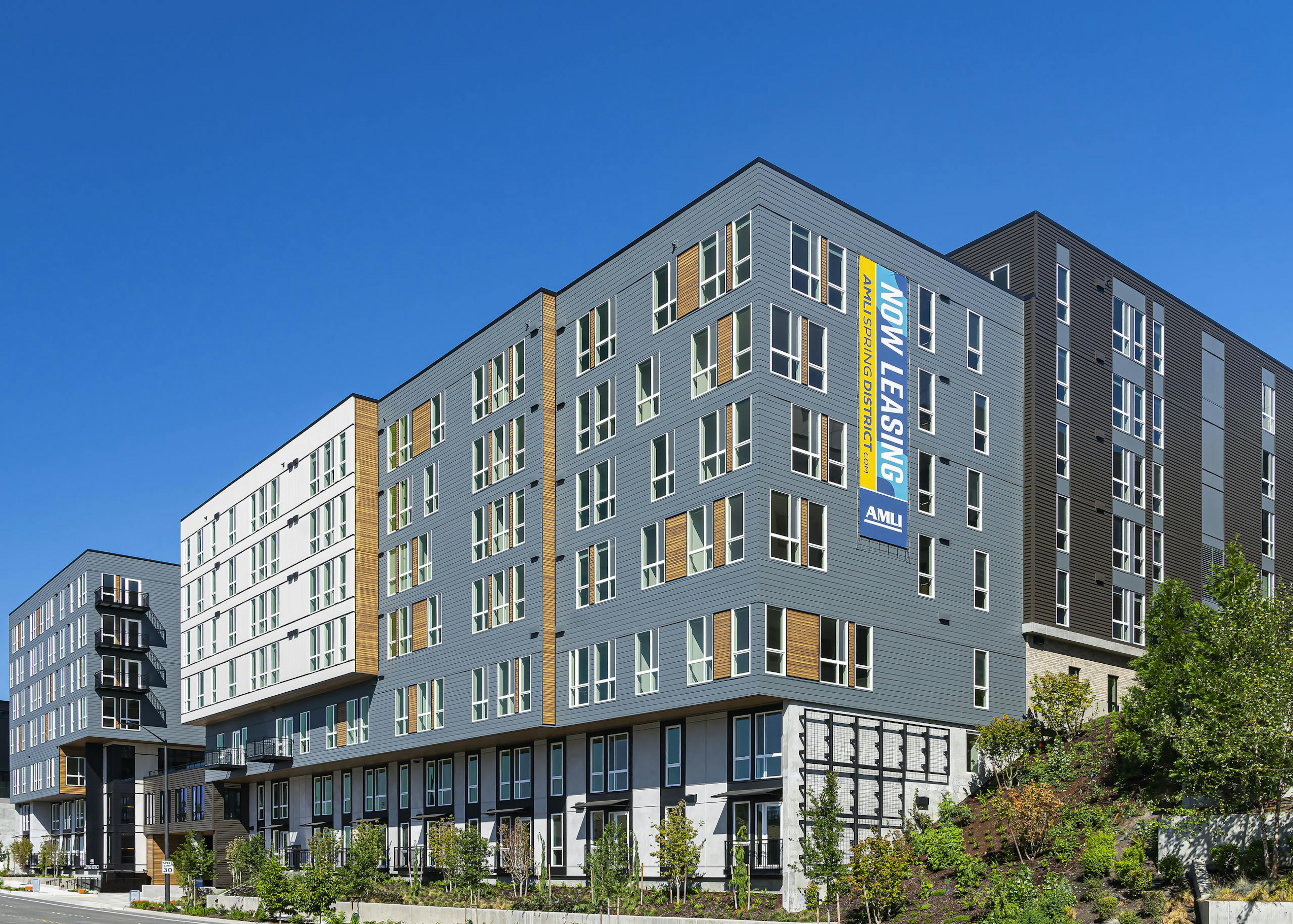 AMLI Spring District blue and brown and white apartment building with wooded highlights and lush landscaping and blue sky