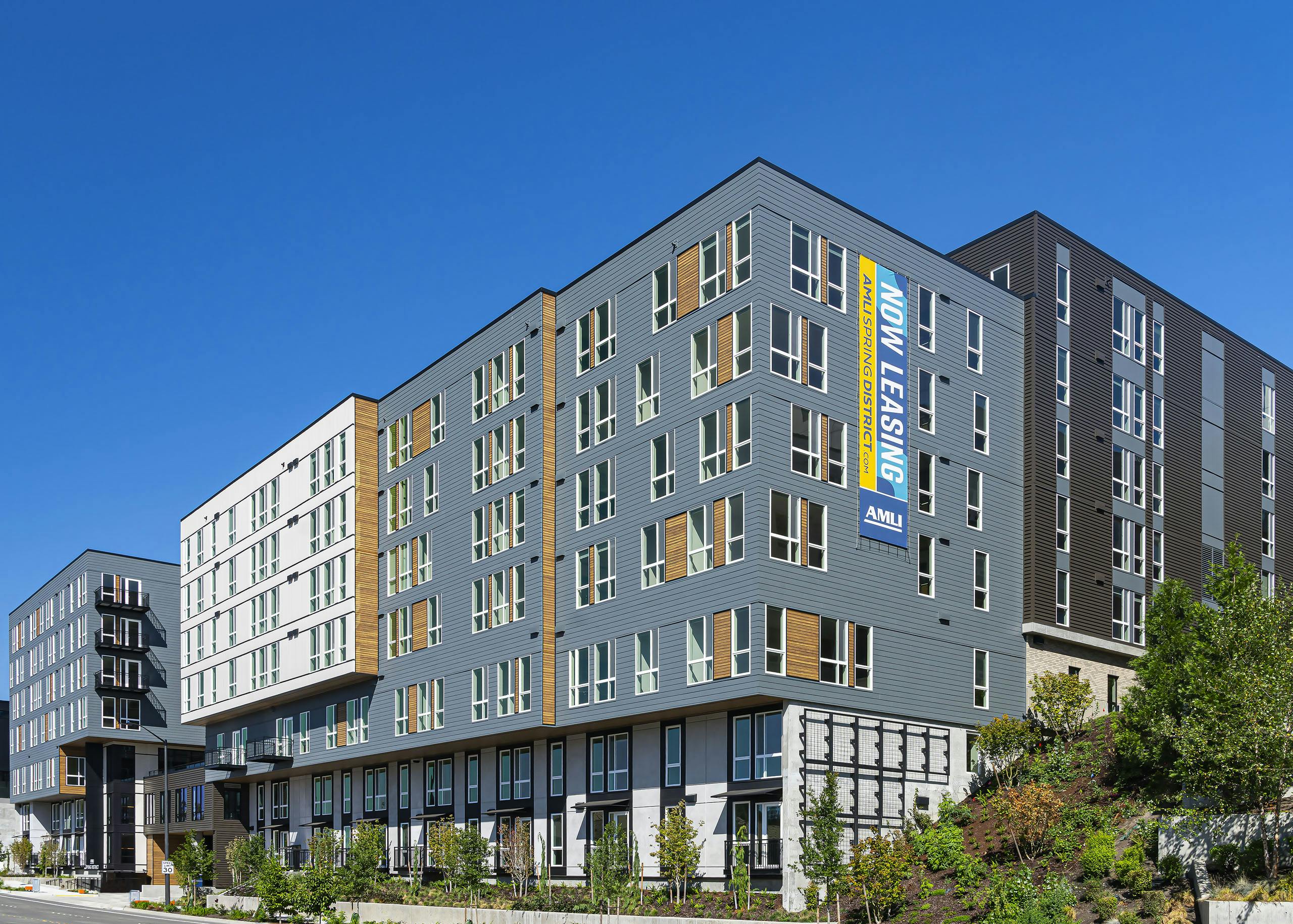 AMLI Spring District blue and brown and white apartment building with wooded highlights and lush landscaping and blue sky