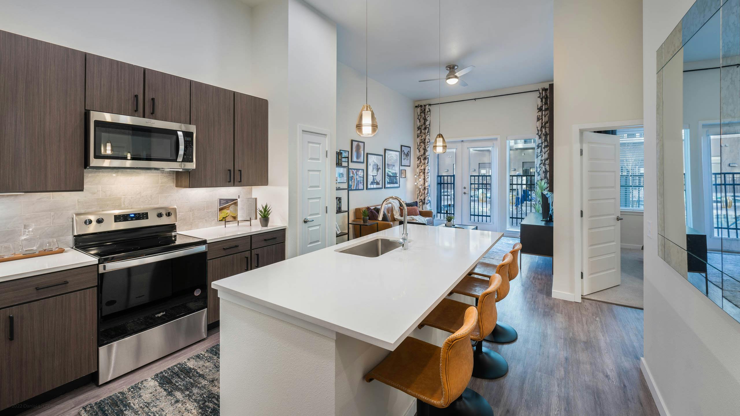 Apartment kitchen at AMLI Art District with white quartz countertops and a tan tile backsplash and a view into the living room