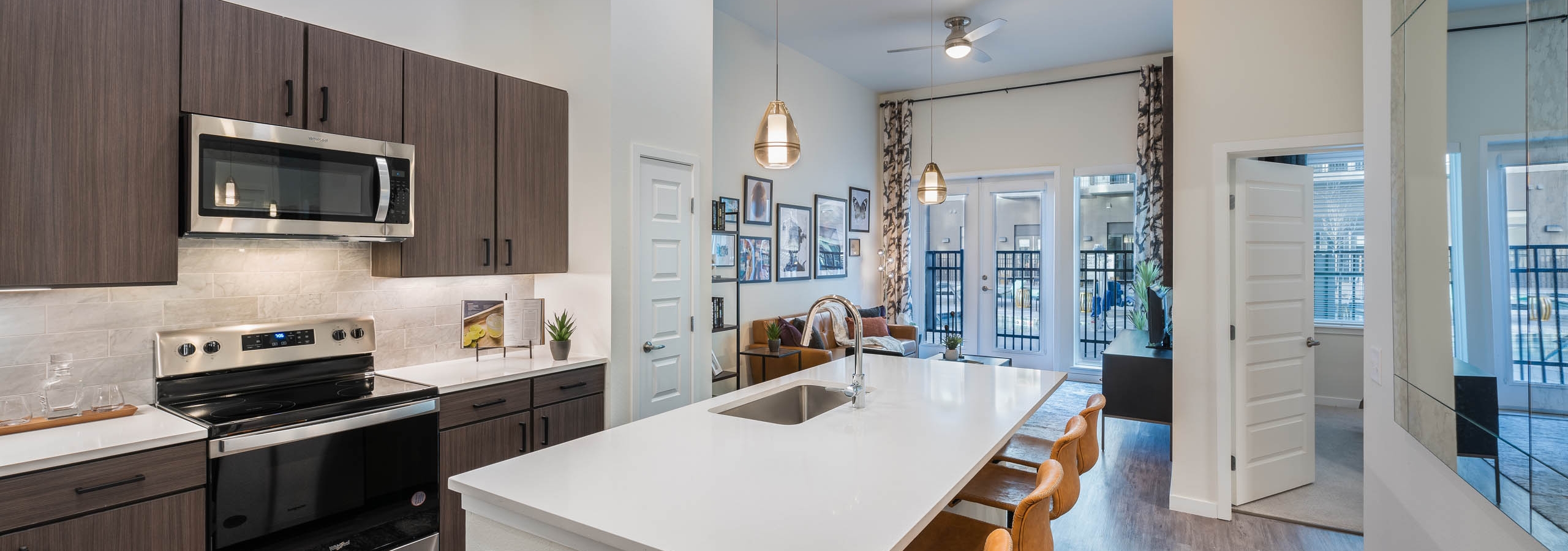 Apartment kitchen at AMLI Art District with white quartz countertops and a tan tile backsplash and a view into the living room
