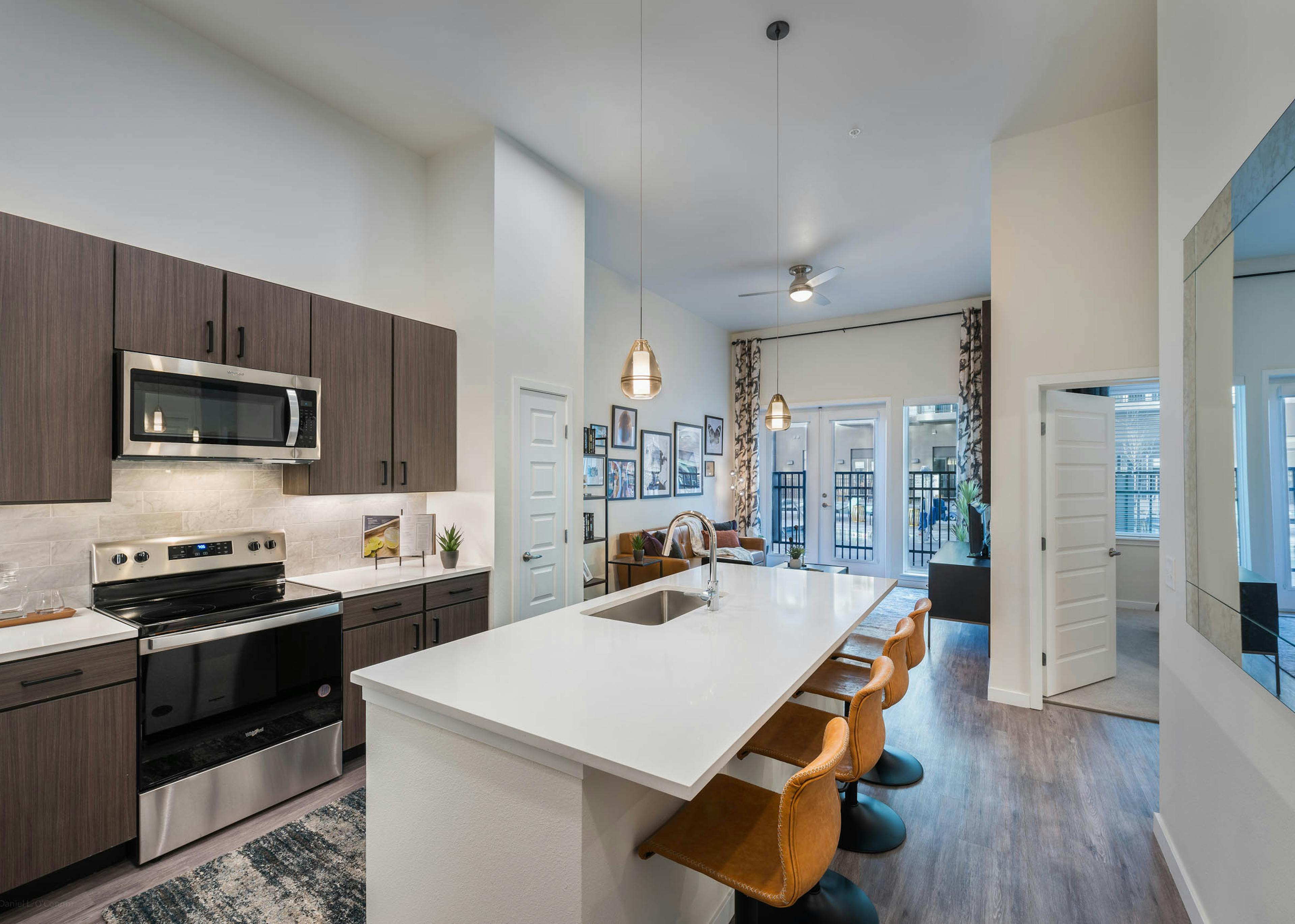 Apartment kitchen at AMLI Art District with white quartz countertops and a tan tile backsplash and a view into the living room 
