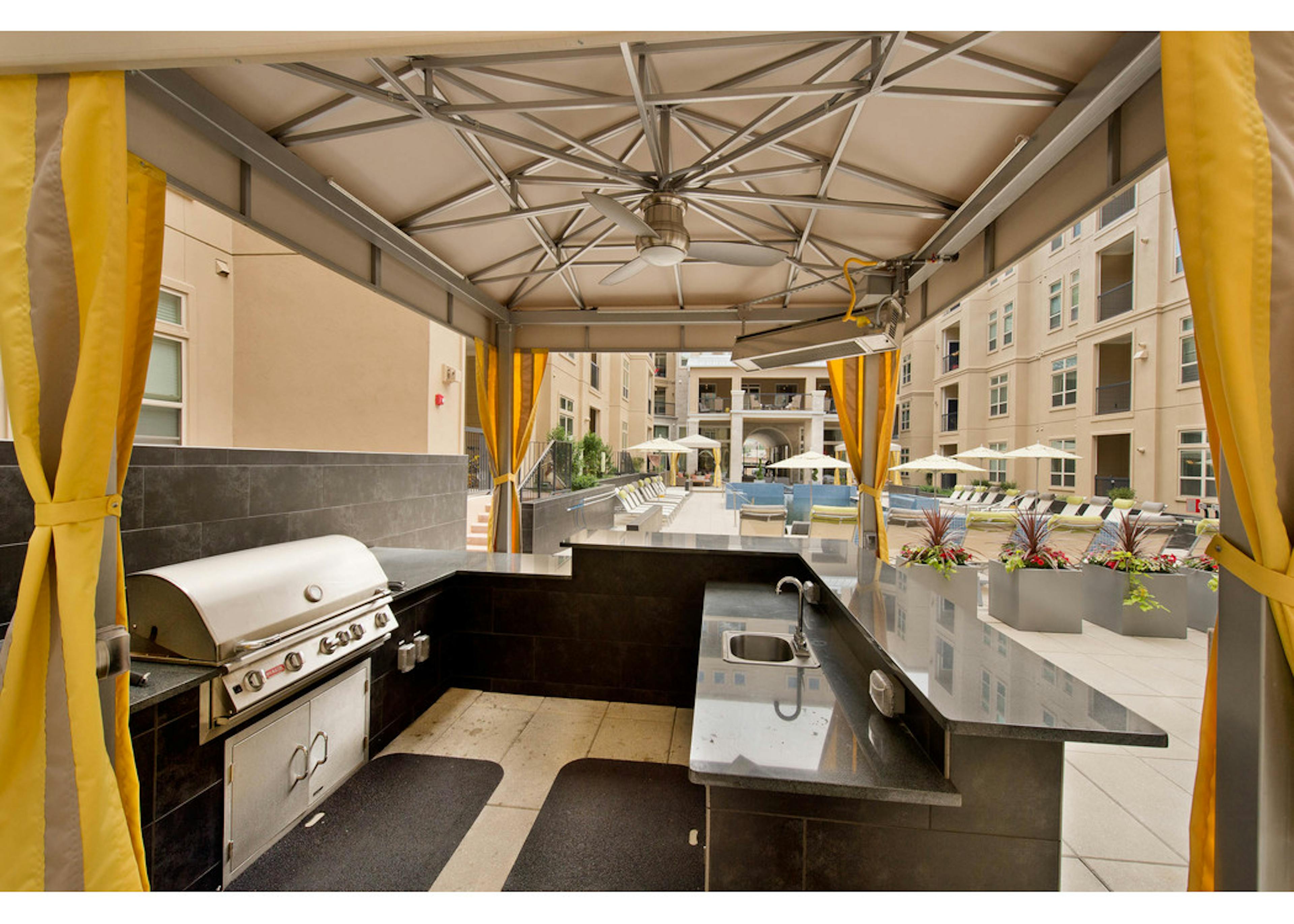 A view of an outdoor kitchen with a cabana at AMLI Ridgegate with a barbecue and a black granite counter top with a sink 