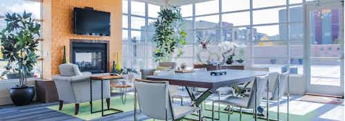Interior view of a clubhouse at AMLI Arista apartments with tables and chairs and plants and a fire place as well as a tv