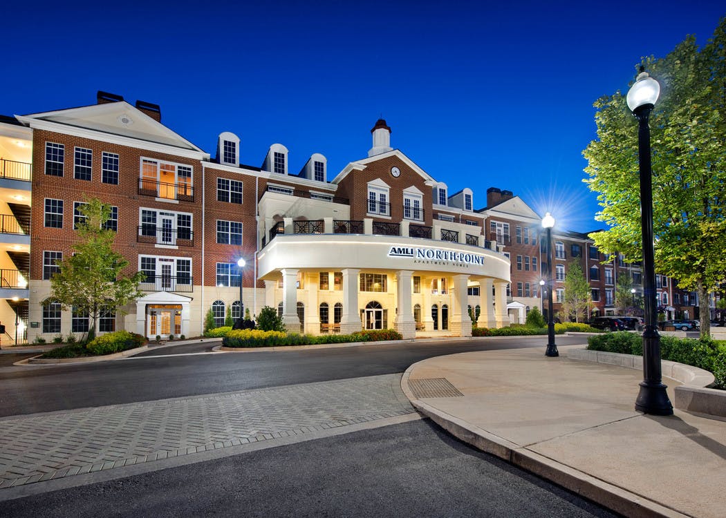 Exterior of AMLI North Point apartment community building at dusk with brick facade and white pillars lining the entry way