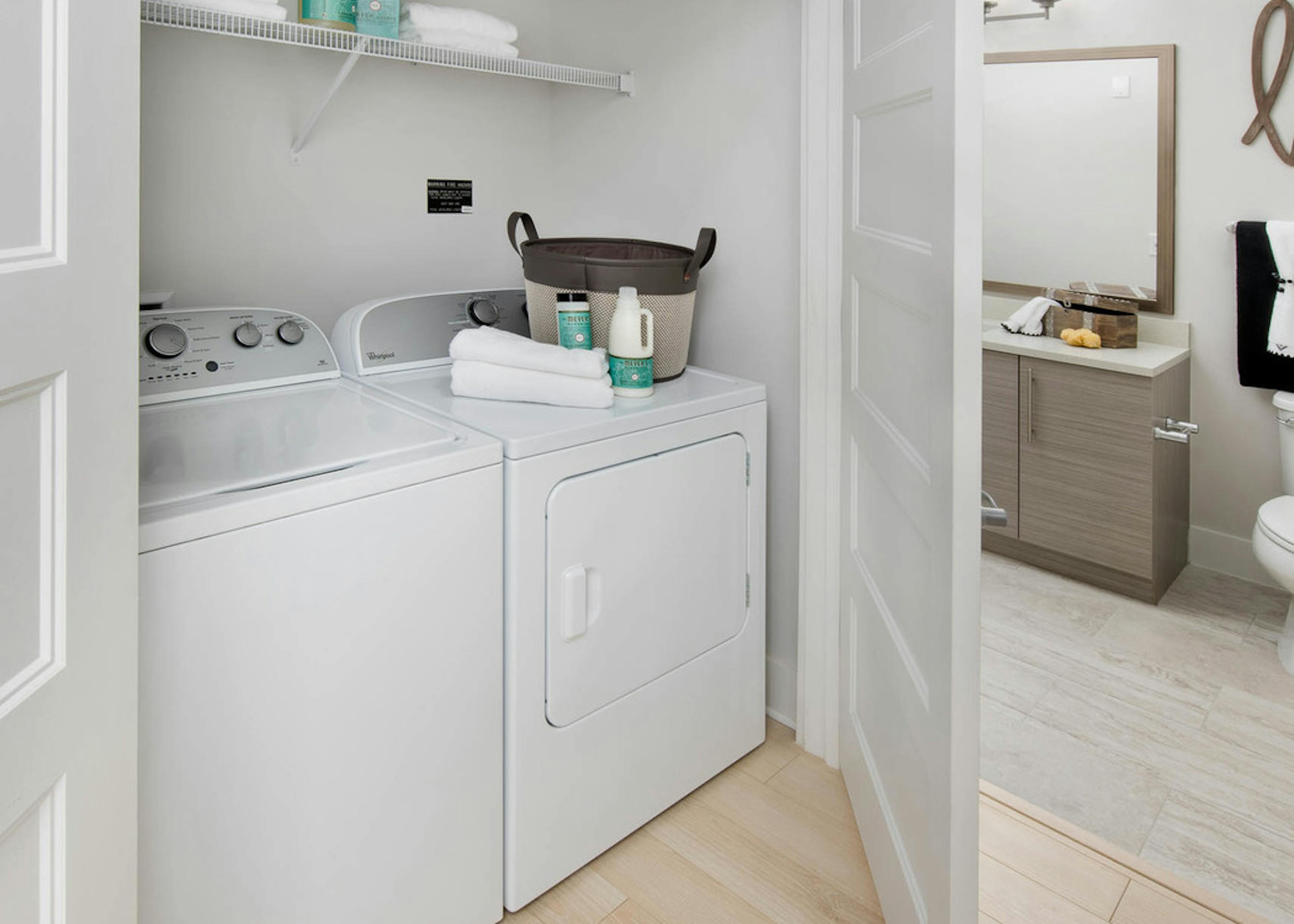 AMLI Buckhead laundry machines with a basket and towel resting on the dryer and a door peaking open leading into the bathroom
