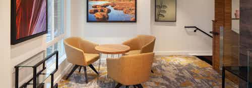 A clubhouse seating area at AMLI Riverfront Green apartments with three chairs and a coffee table with multiple art pieces