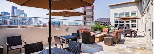 Exterior view of the sky deck at AMLI Park Avenue apartments with several tables and chairs and umbrellas and Denver skyline