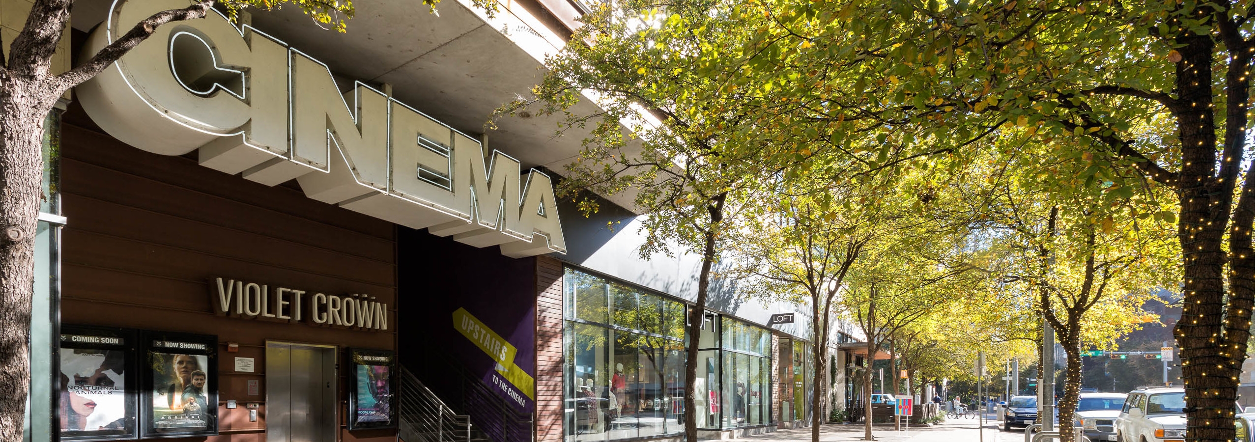 Close up of Cinema storefront in the 2nd street district with other storefronts and thriving green trees in the background