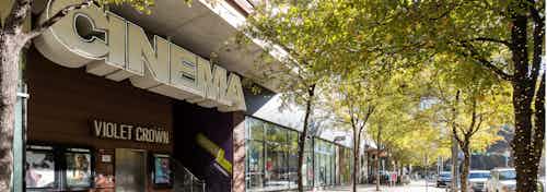 Close up of Cinema storefront in the 2nd street district with other storefronts and thriving green trees in the background