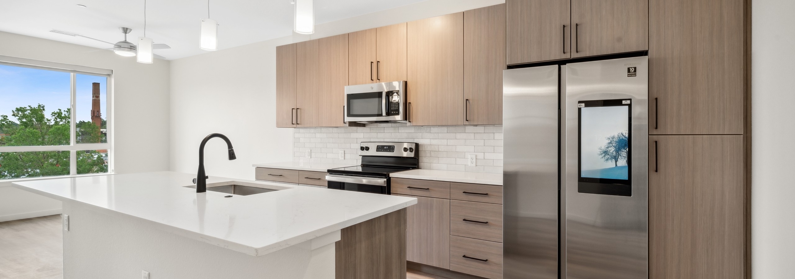 AMLI Broadway Park apartment kitchen with island and white countertop with white pendant lighting and built-in stainless refrigerator