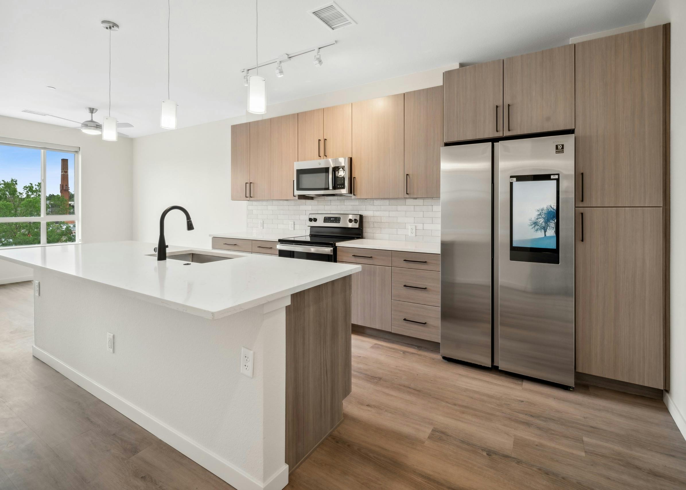 AMLI Broadway Park apartment kitchen with island and white countertop with white pendant lighting and built-instainless  refrigerator