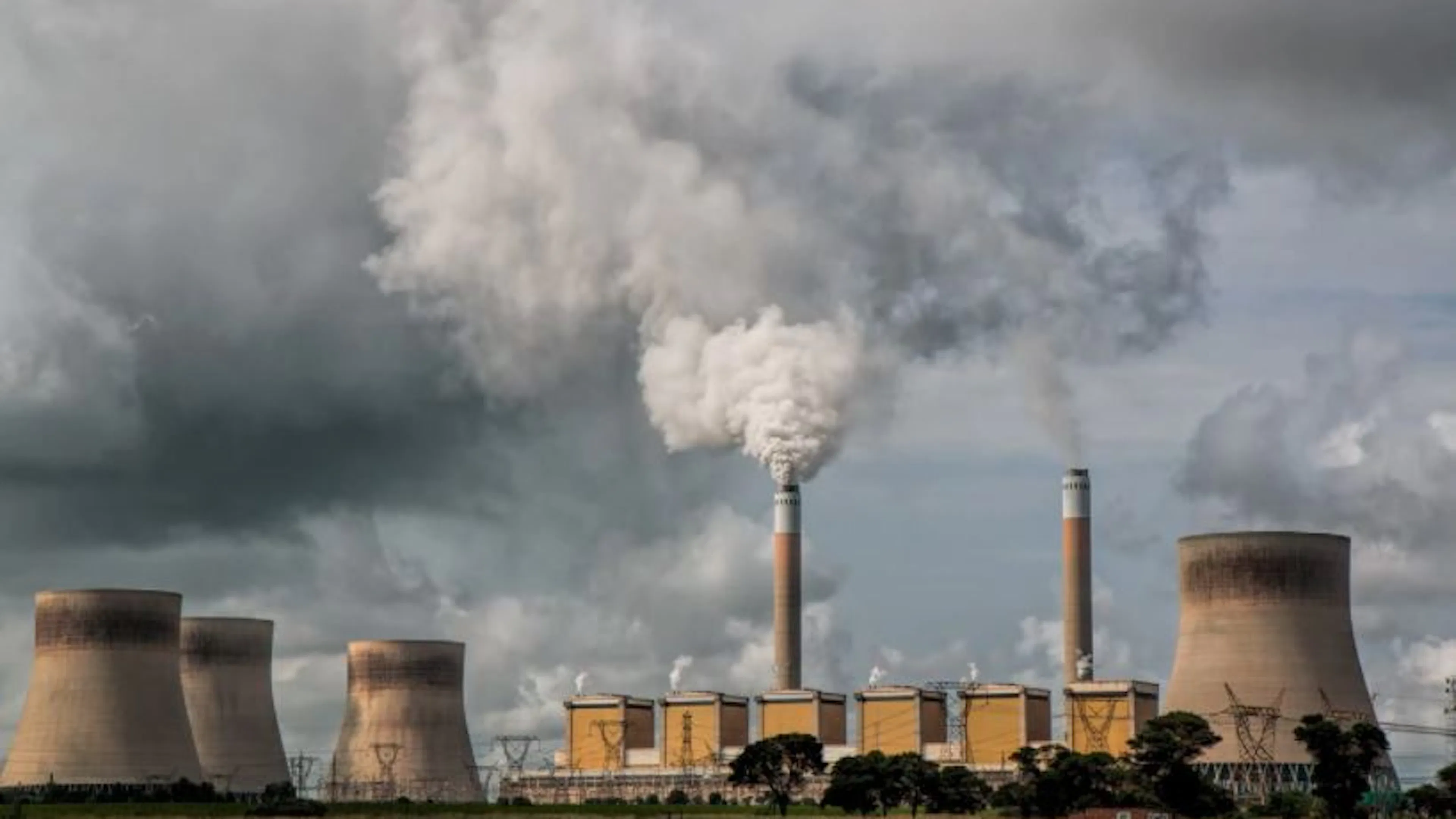 A wide landscape shot of large and small smokestacks spouting steam into a cloudy sky