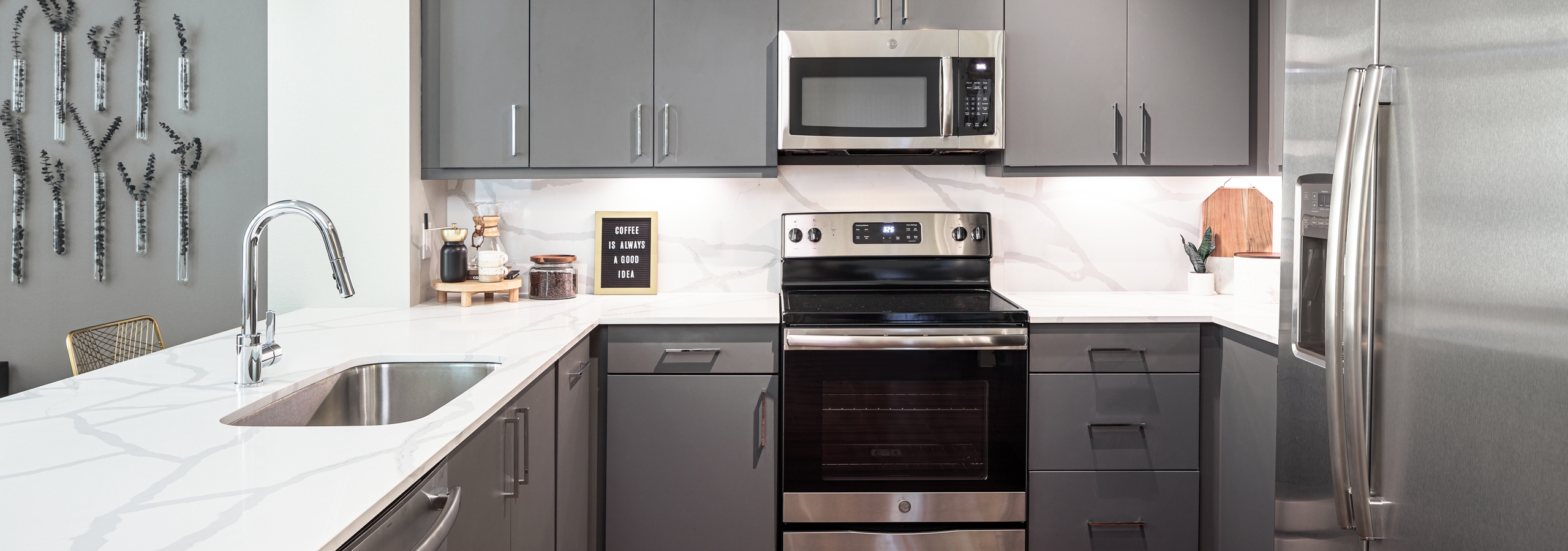 Interior view of AMLI Addison kitchen with grey cabinets and quartz countertops and backsplash with peek into living area