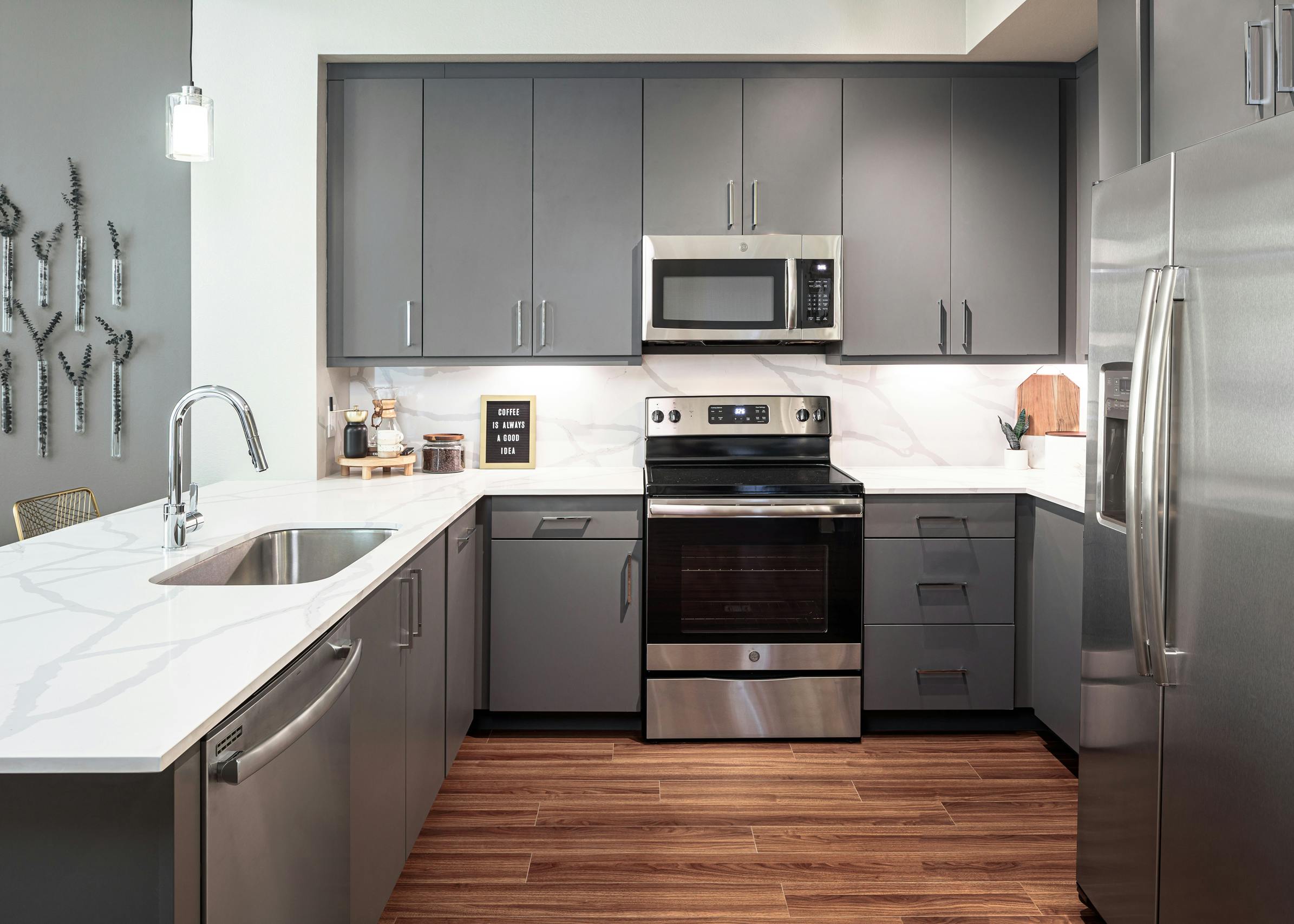 Interior view of AMLI Addison kitchen with grey cabinets and quartz countertops and backsplash with peek into living area