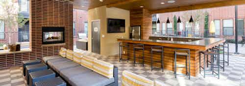 Close up of brick fireplace in the AMLI West Plano outdoor kitchen with nearby barstool and couch seating options