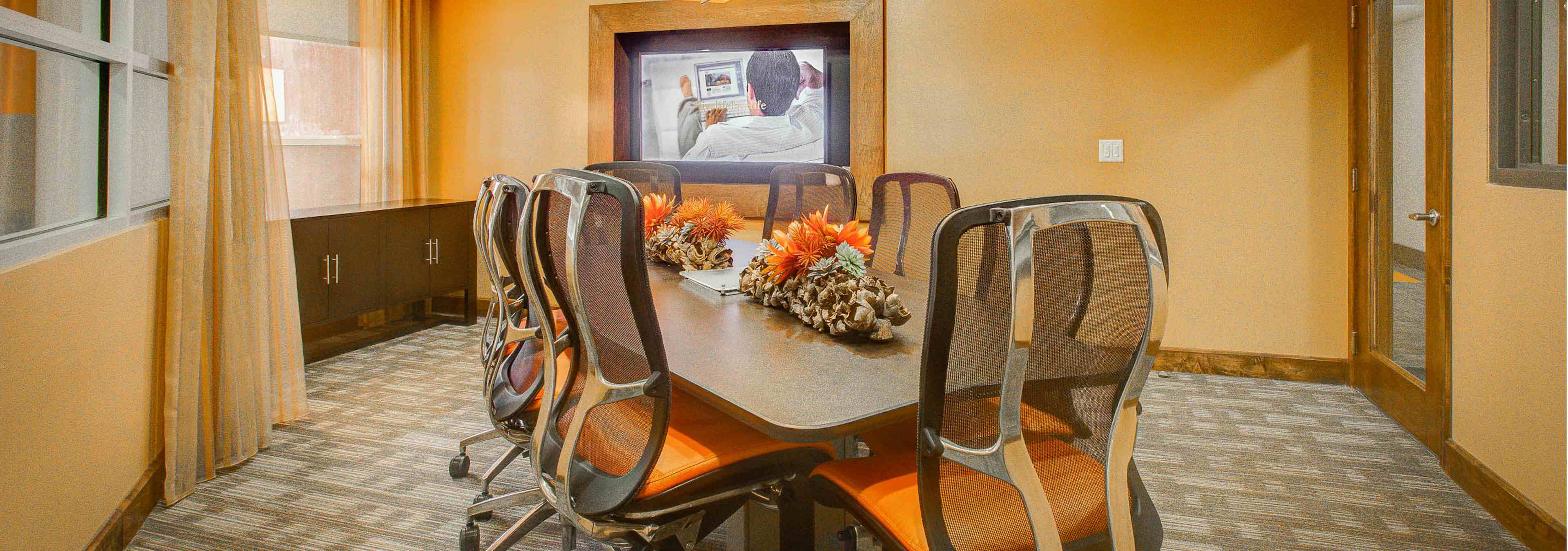 Interior view of a conference room at AMLI Riverfront Park apartments with a long table with rolling chairs and a television