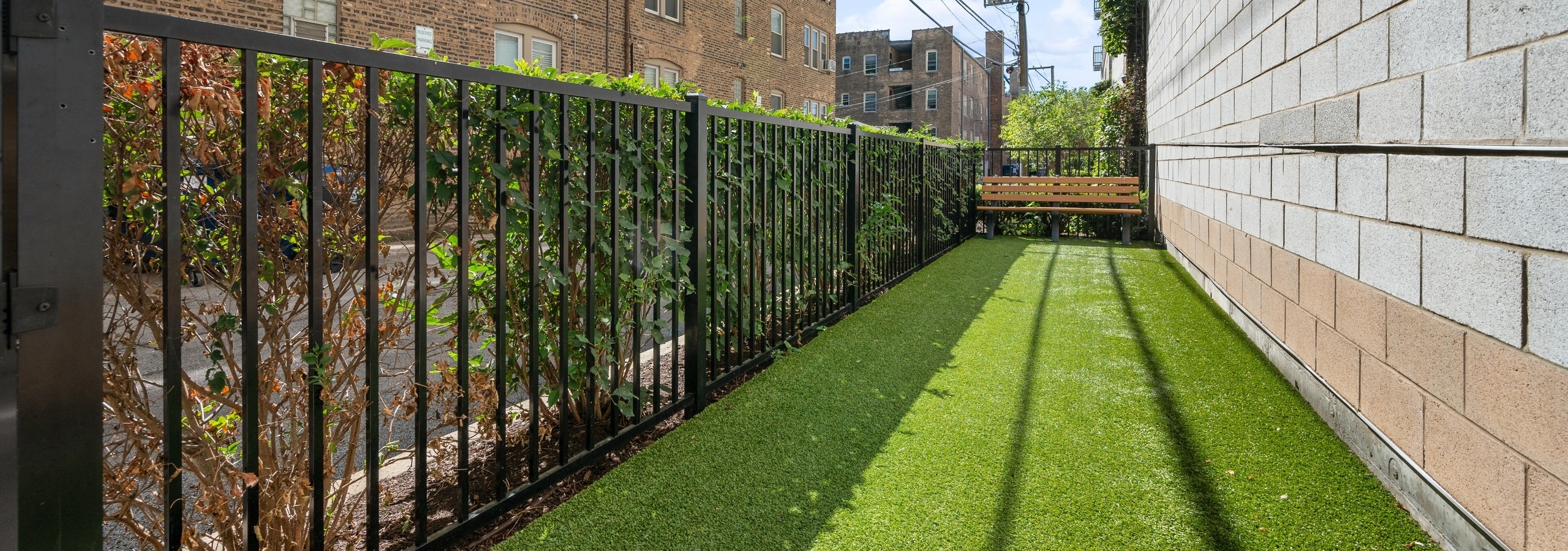 AMLI Evanston pet park with green turf and bench and  black fence opposite a concrete wall facing adjacent building