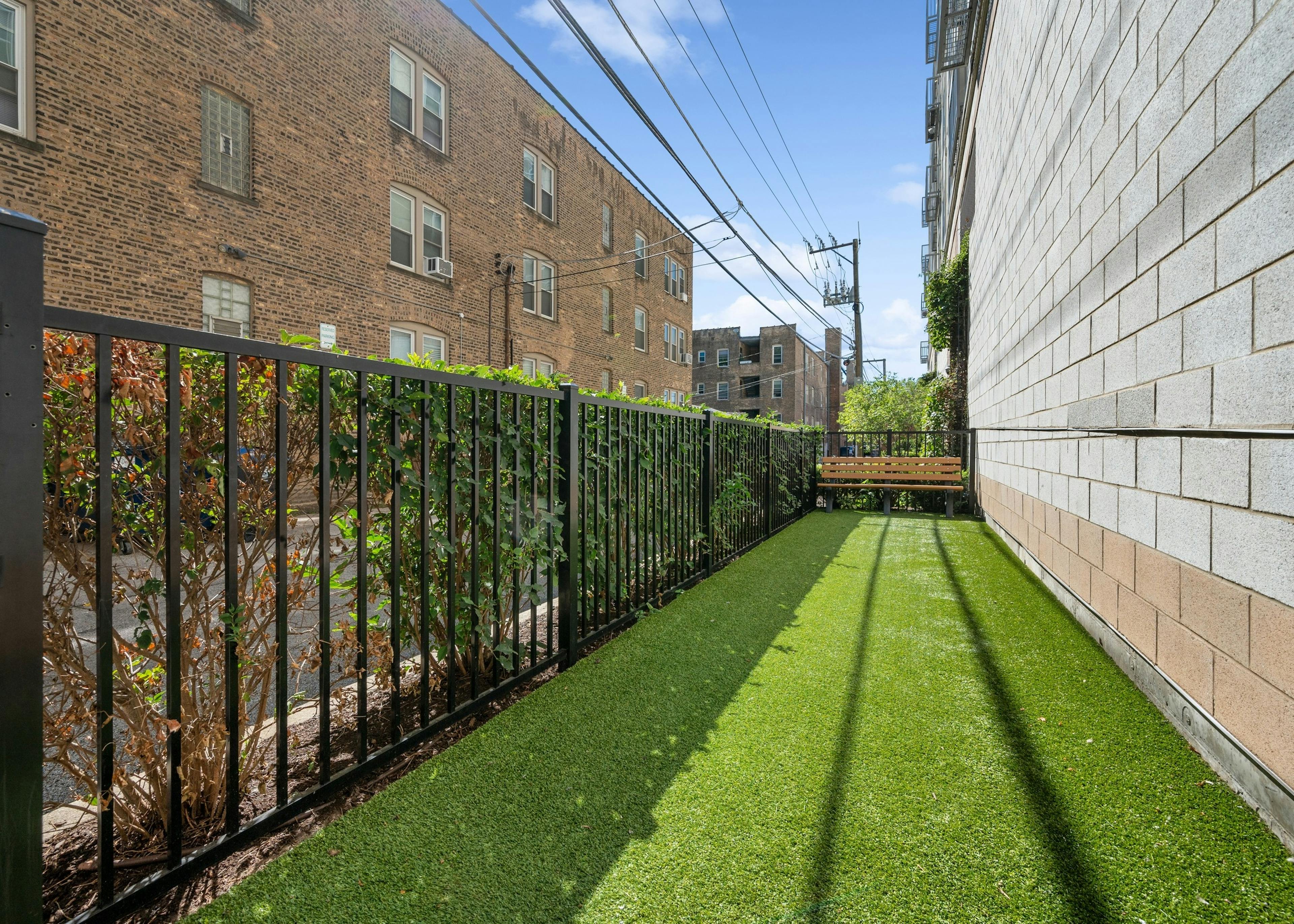 AMLI Evanston pet park with green turf and bench and  black fence opposite a concrete wall facing adjacent building