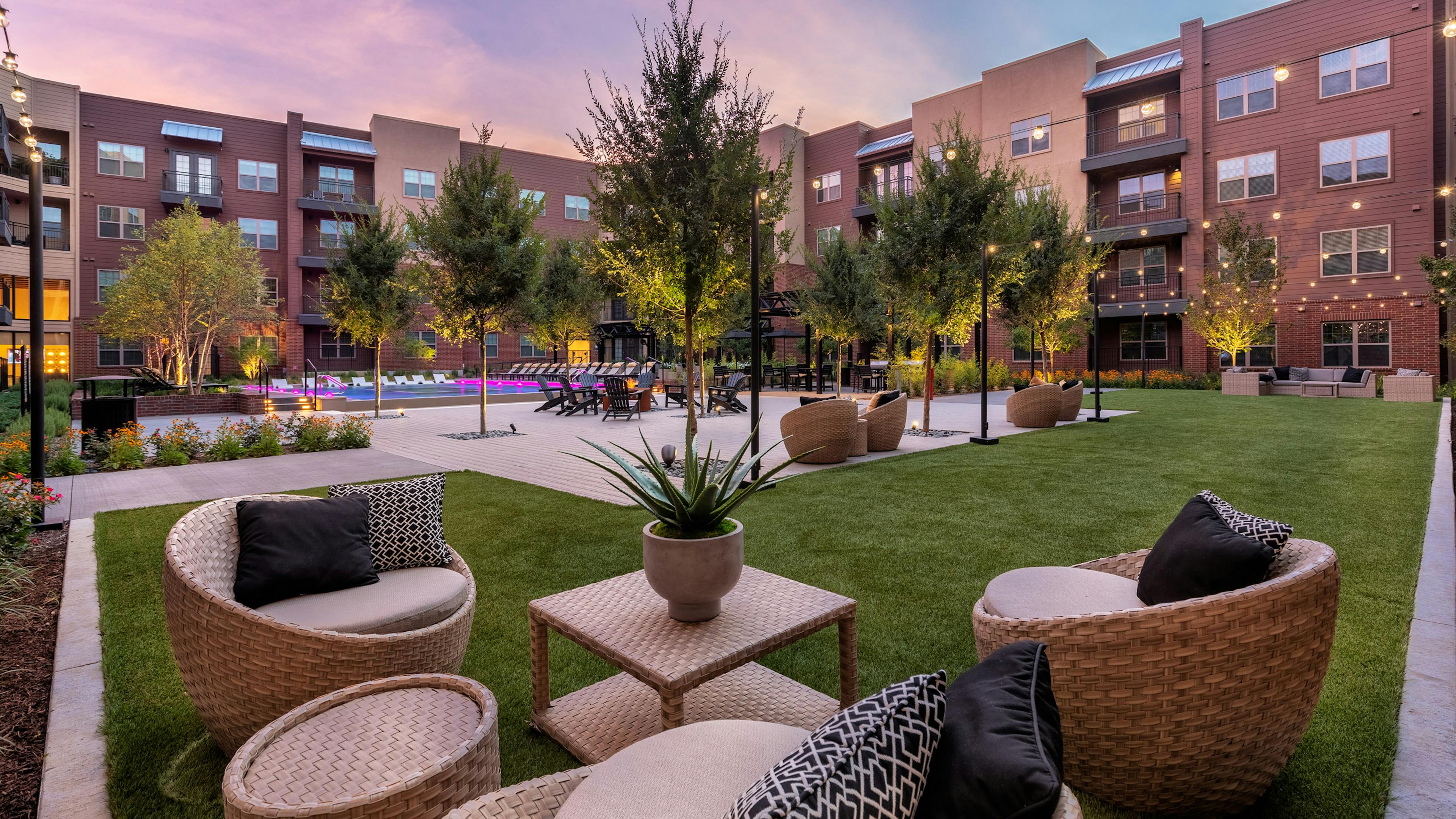 Dusk view of AMLI Grapevine outdoor living room with wicker chairs and tables on grass in courtyard with pool in background