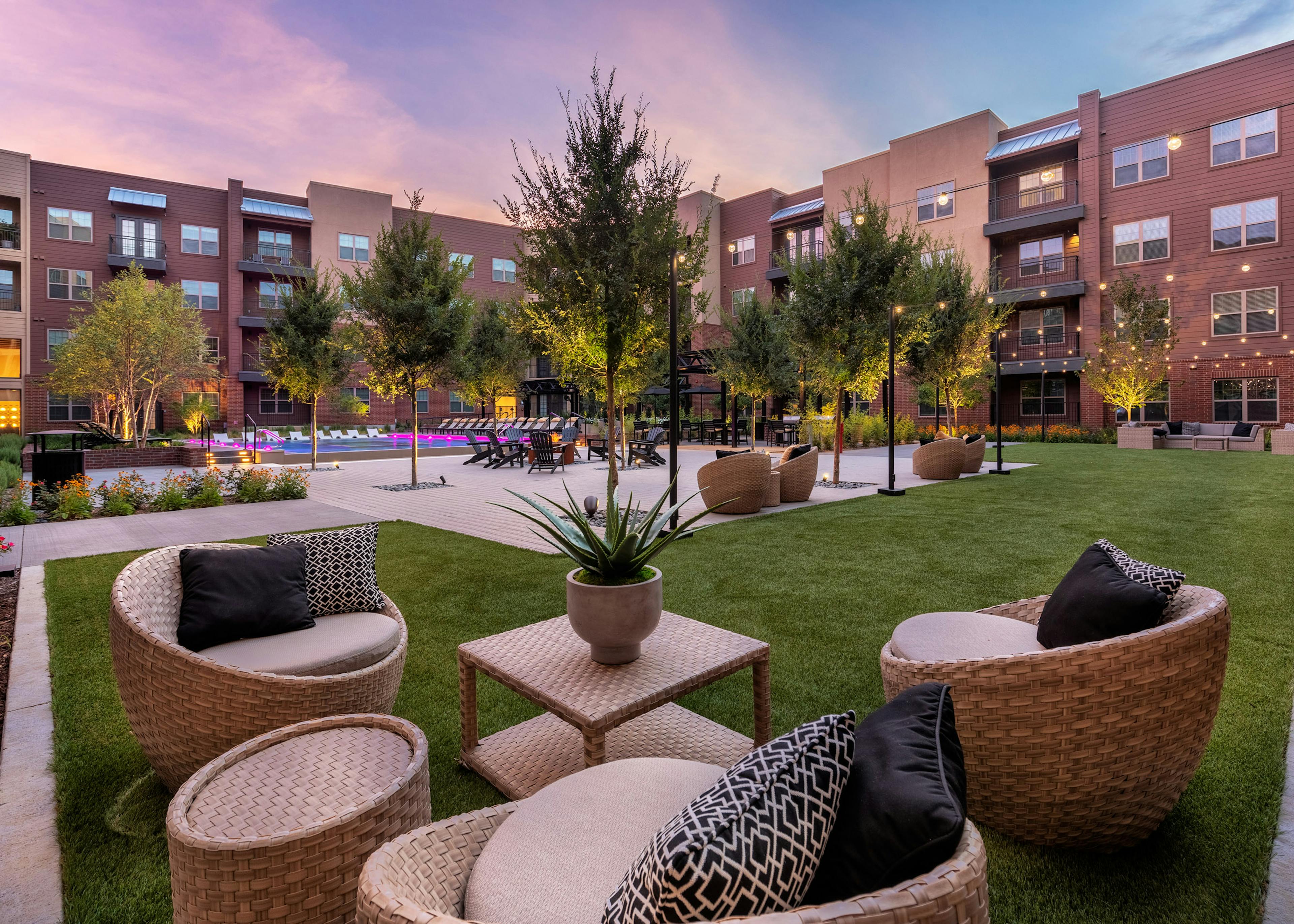 Dusk view of AMLI Grapevine outdoor living room with wicker chairs and tables on grass in courtyard with pool in background