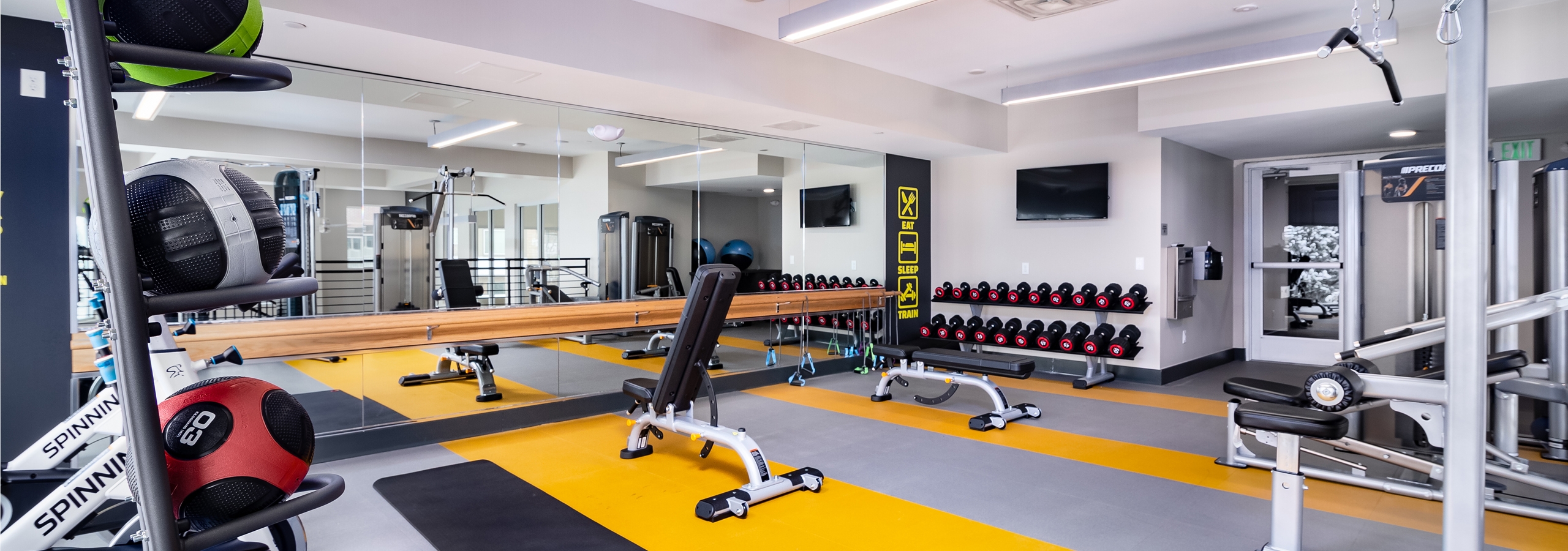 Interior view of fitness center at AMLI Littleton Village apartments with free weights, medicine balls and big screen TV