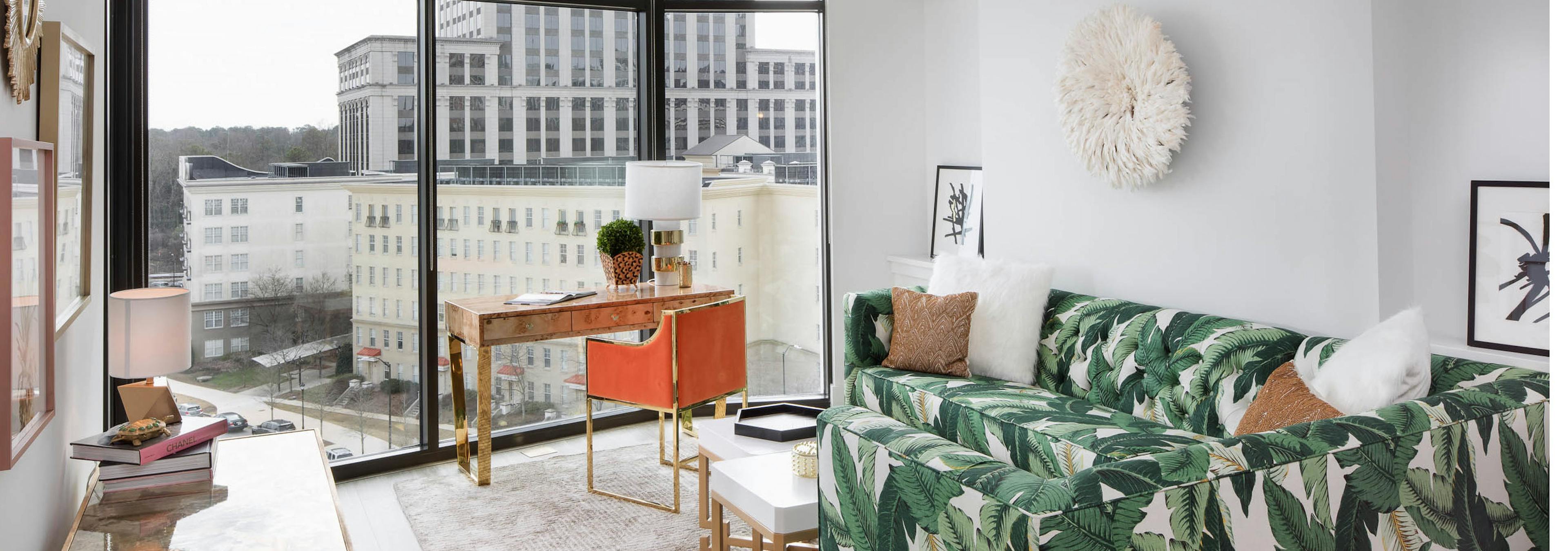 Interior of AMLI 3464 living room with white walls and floor to ceiling windows with a bold palm tree branch printed sofa