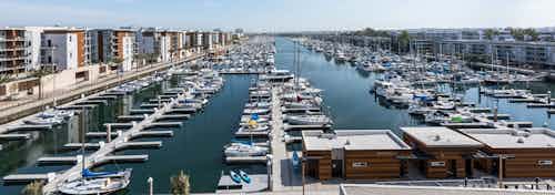 Daytime aerial view of the marina, boat slips with boats and boat houses and part of AMLI Marina Del Rey apartment buildings