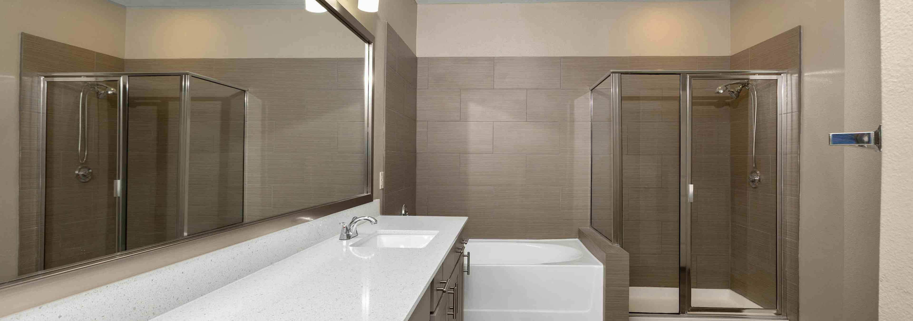 Interior of AMLI Eastside bathroom with a glass shower and separate bathtub with a spacious white countertop vanity sink