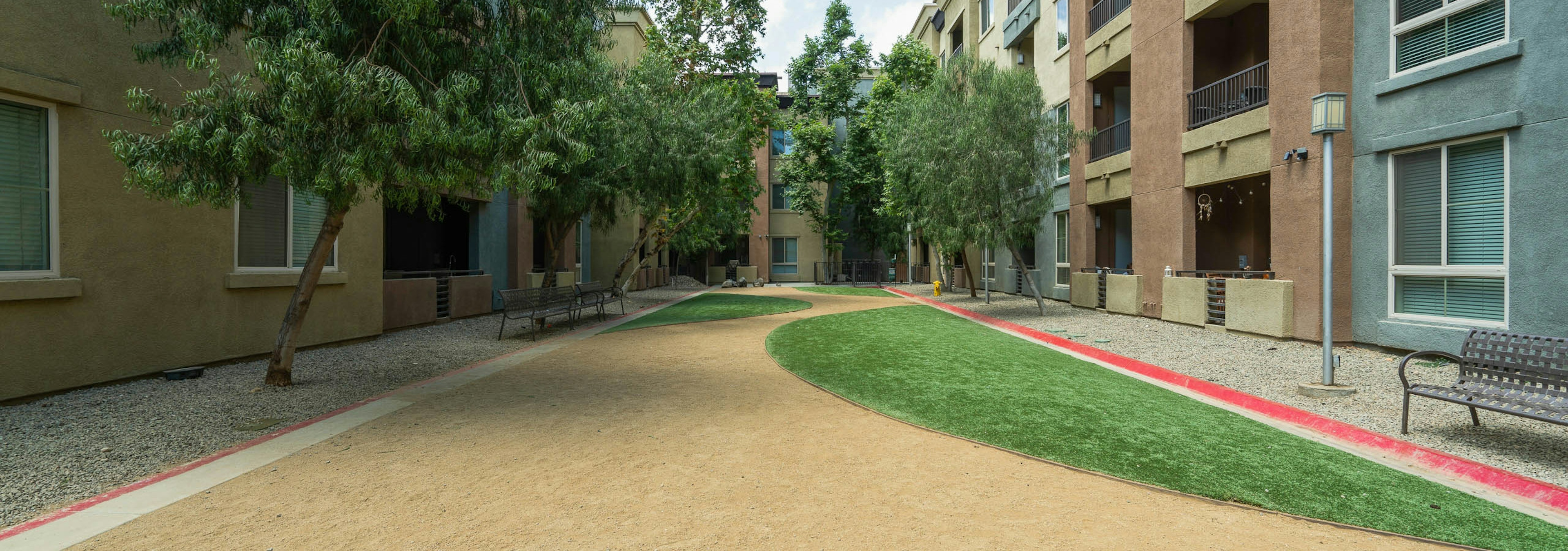 Daytime view of Dog Park with grass, benches and bed of rocks surrounded by trees at AMLI Warner Center apartment building