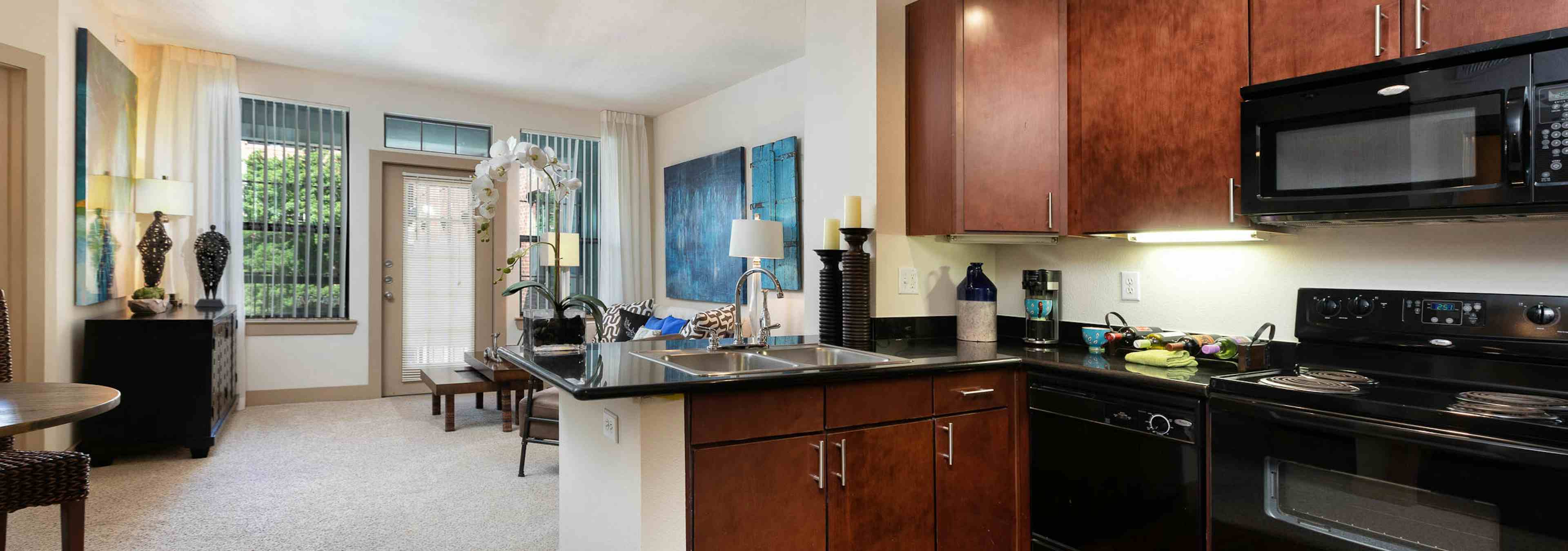 Kitchen at AMLI Eastside with cherry cabinets and black countertops with black appliances and a view of carpeted living area