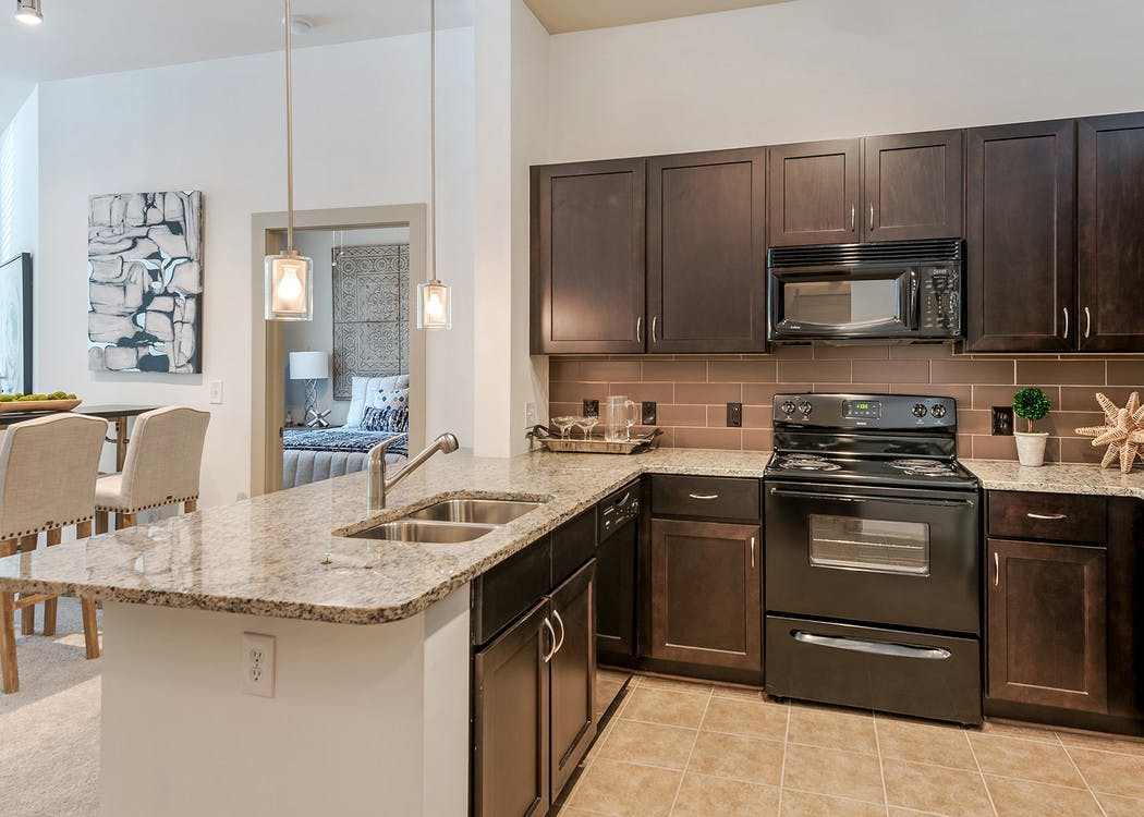 AMLI Parkside apartment spacious kitchen with light tile and dark cabinetry and black appliances with peek into living room