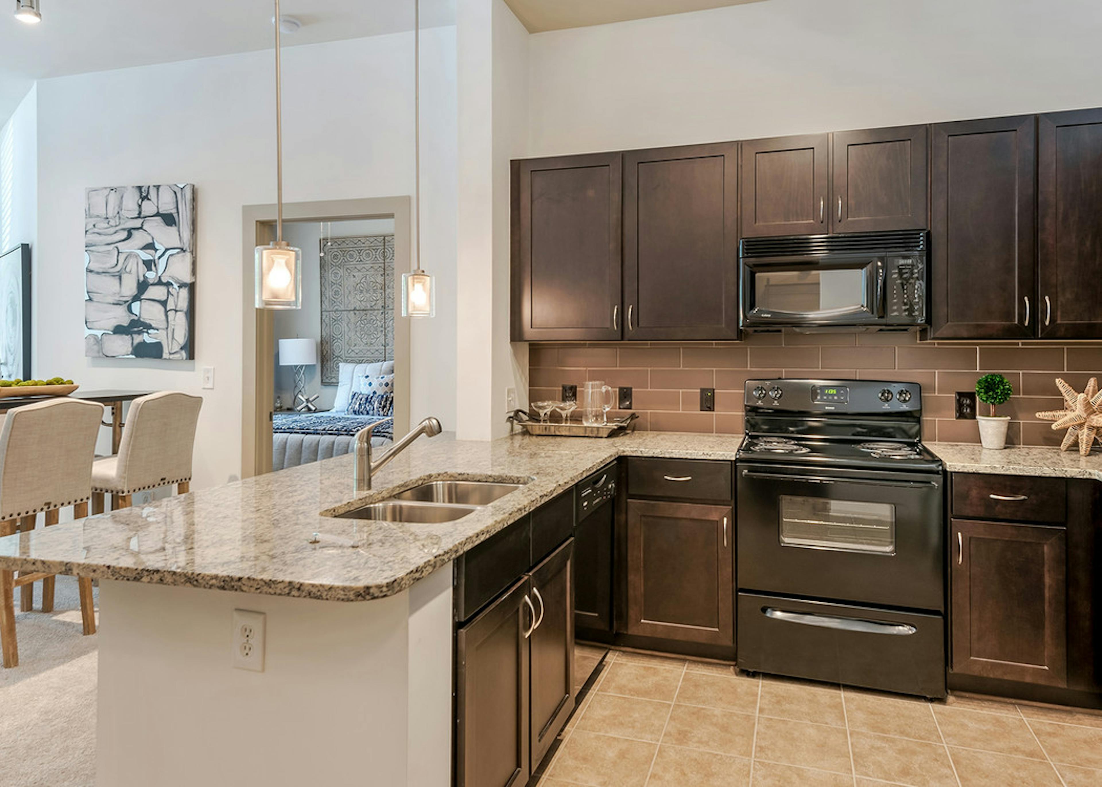 AMLI Parkside apartment spacious kitchen with light tile and dark cabinetry and black appliances with peek into living room