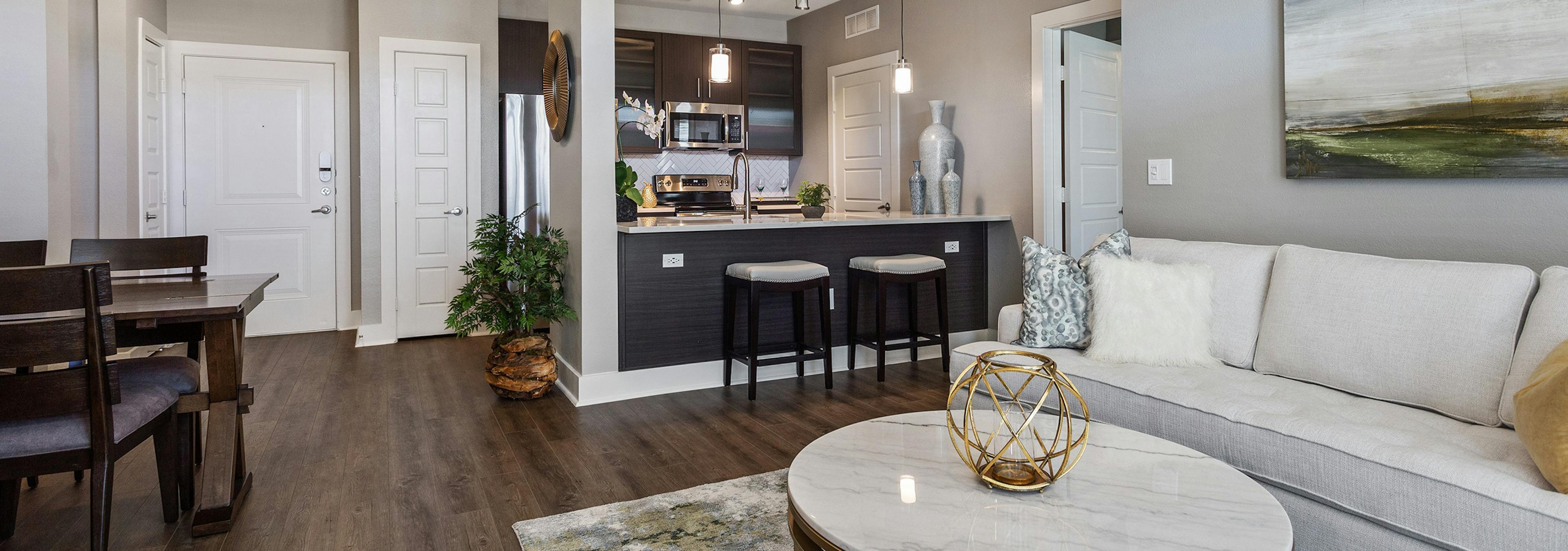 Living room at AMLI South Shore with dark hardwood and light walls with a white sofa and view of stools at kitchen counter