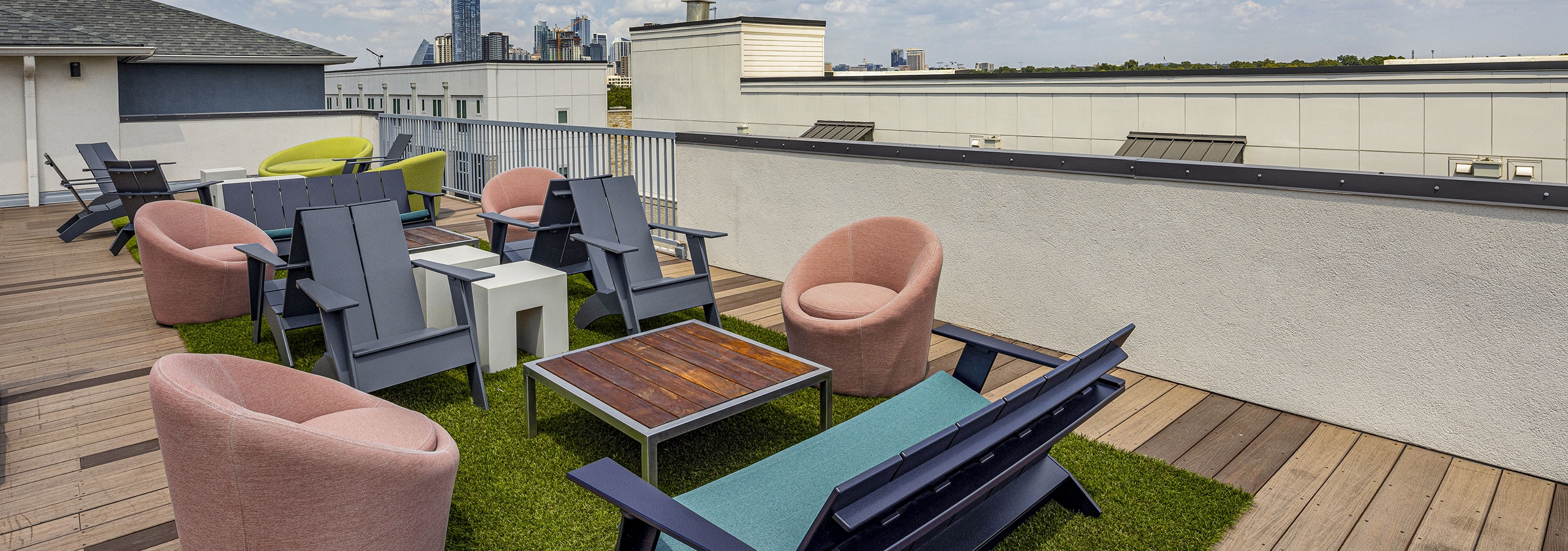 Exterior view of roof deck at AMLI South Shore with gray and Adirondack chairs and couch and soft pink chairs around brown table