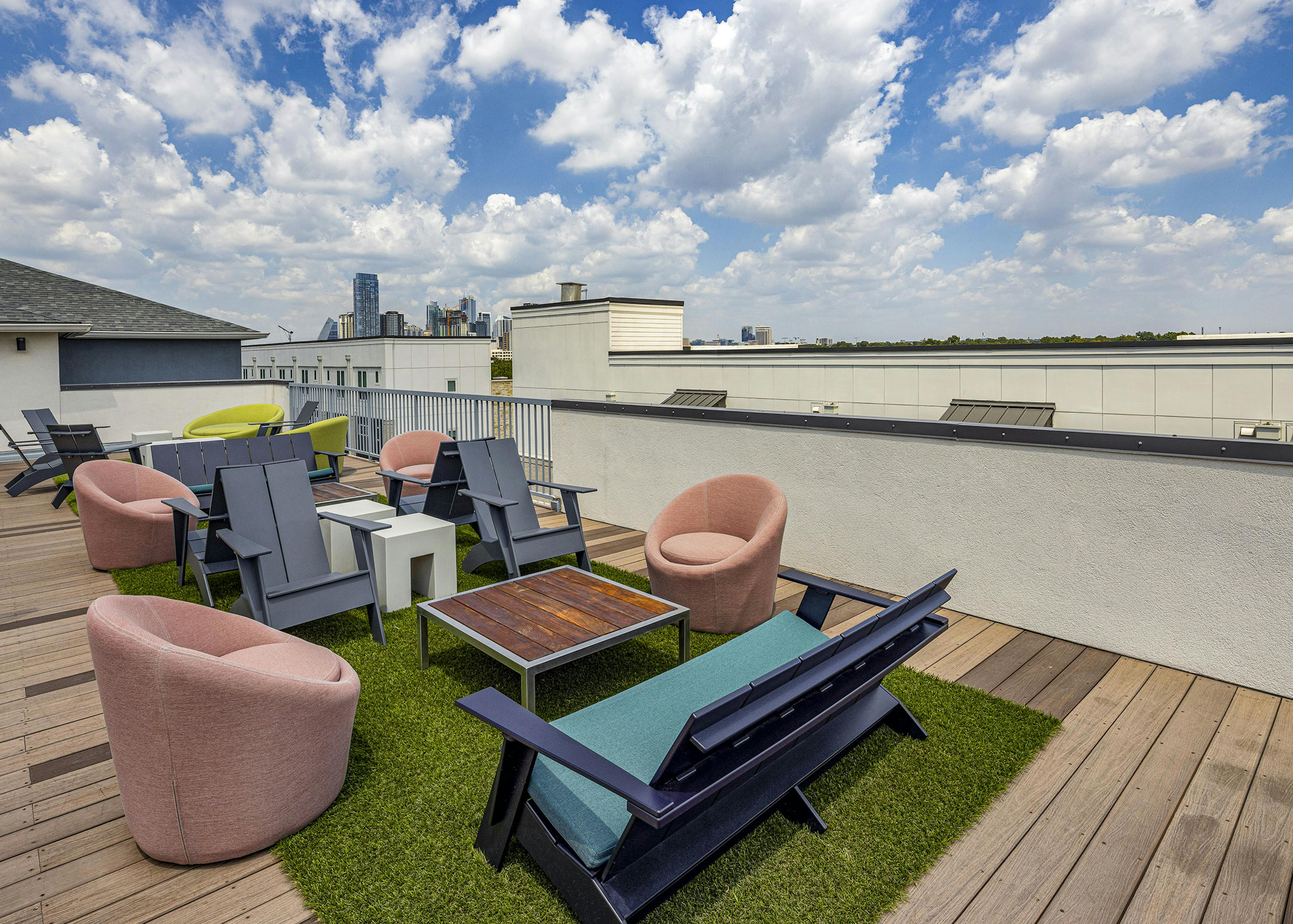 Exterior view of roof deck at AMLI South Shore with gray and Adirondack chairs and couch and soft pink chairs around brown table 