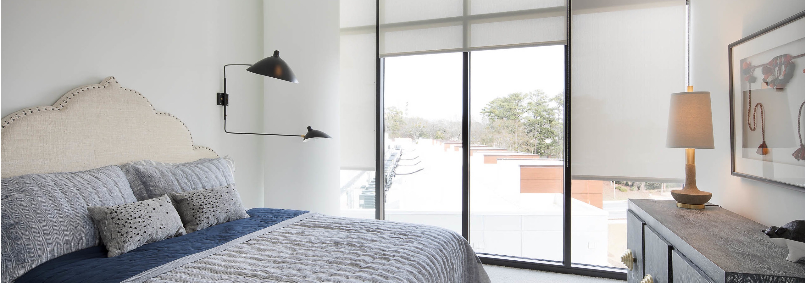Bedroom at AMLI 3464 with white walls and grey and dark blue bedding with floor to ceiling windows with a daytime view