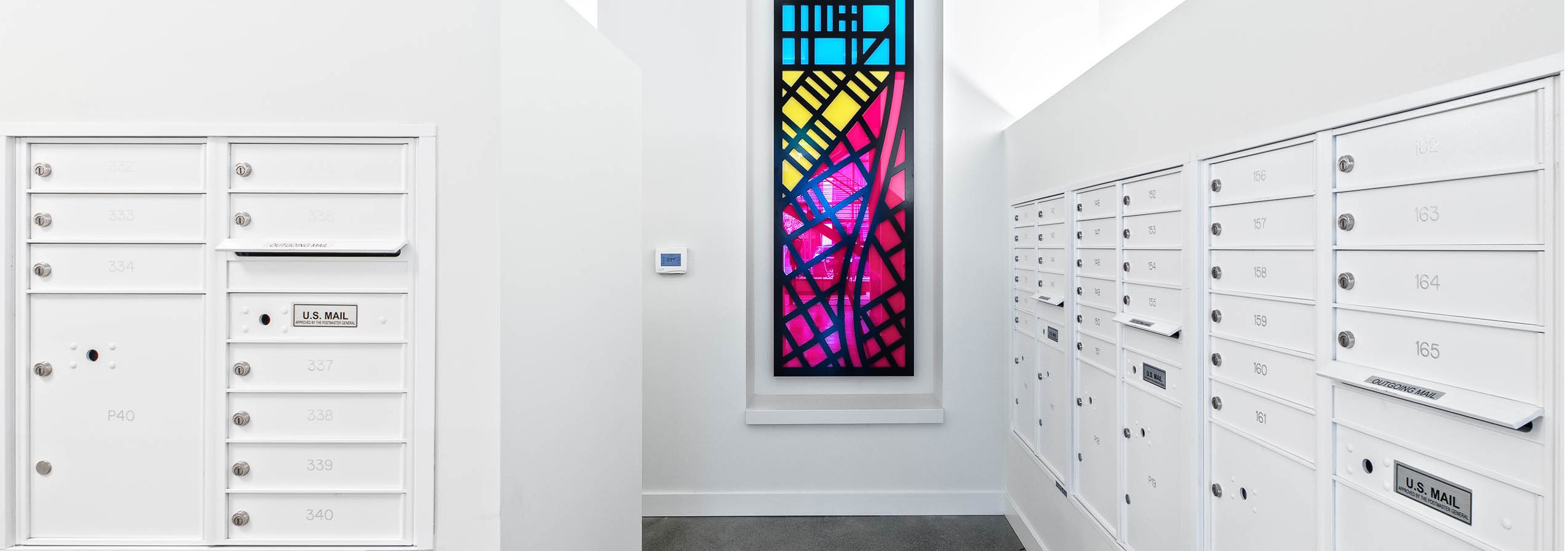 Interior mail room of AMLI Arc with white mail boxes white walls and a colorful stain glass art piece hanging on the wall