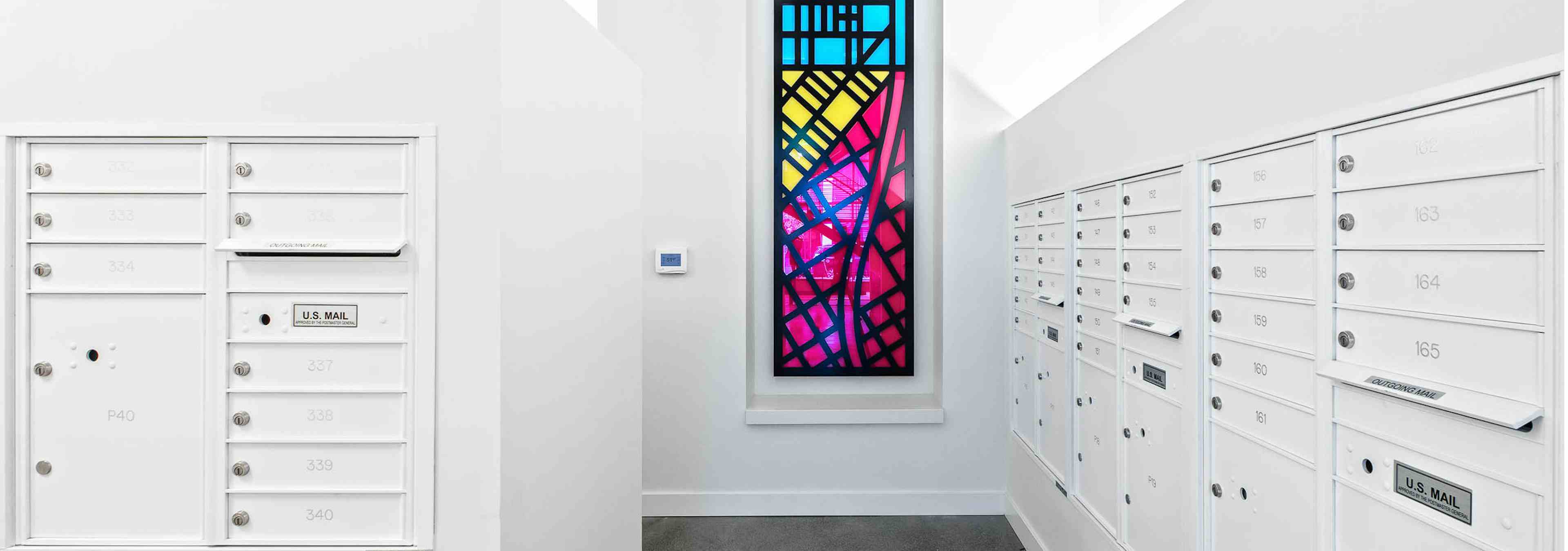 Interior mail room of AMLI Arc with white mail boxes white walls and a colorful stain glass art piece hanging on the wall 