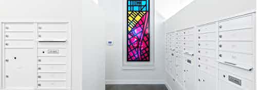 Interior mail room of AMLI Arc with white mail boxes white walls and a colorful stain glass art piece hanging on the wall